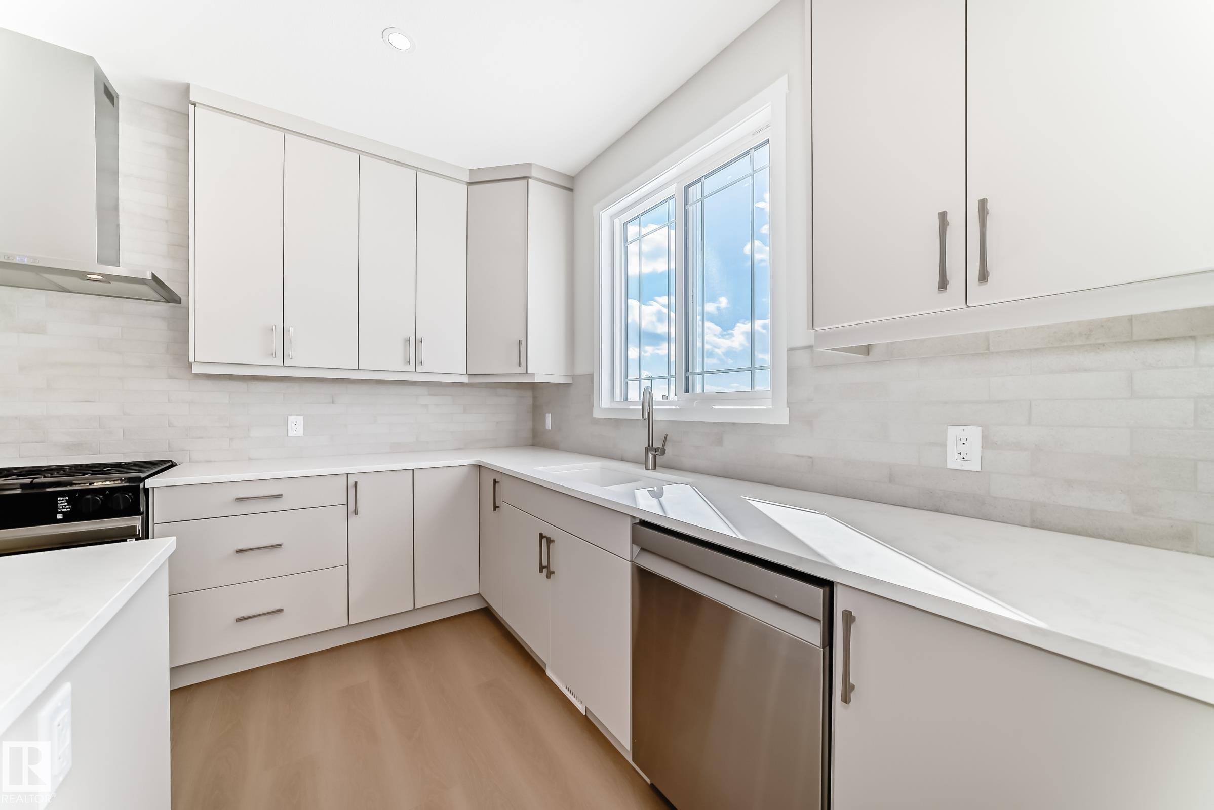 The kitchen features light-colored cabinetry, a modern range hood, a stainless steel dishwasher, and a window above the sink - 1516 206 Street Nw, Edmonton, AB - Indoor Photo Showing Kitchen