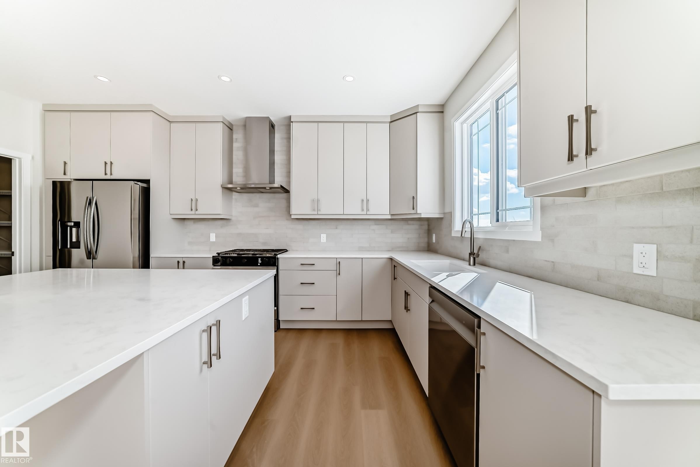 The property features a kitchen with light-toned cabinetry, stainless steel appliances, and a large central island - 1516 206 Street Nw, Edmonton, AB - Indoor Photo Showing Kitchen With Upgraded Kitchen