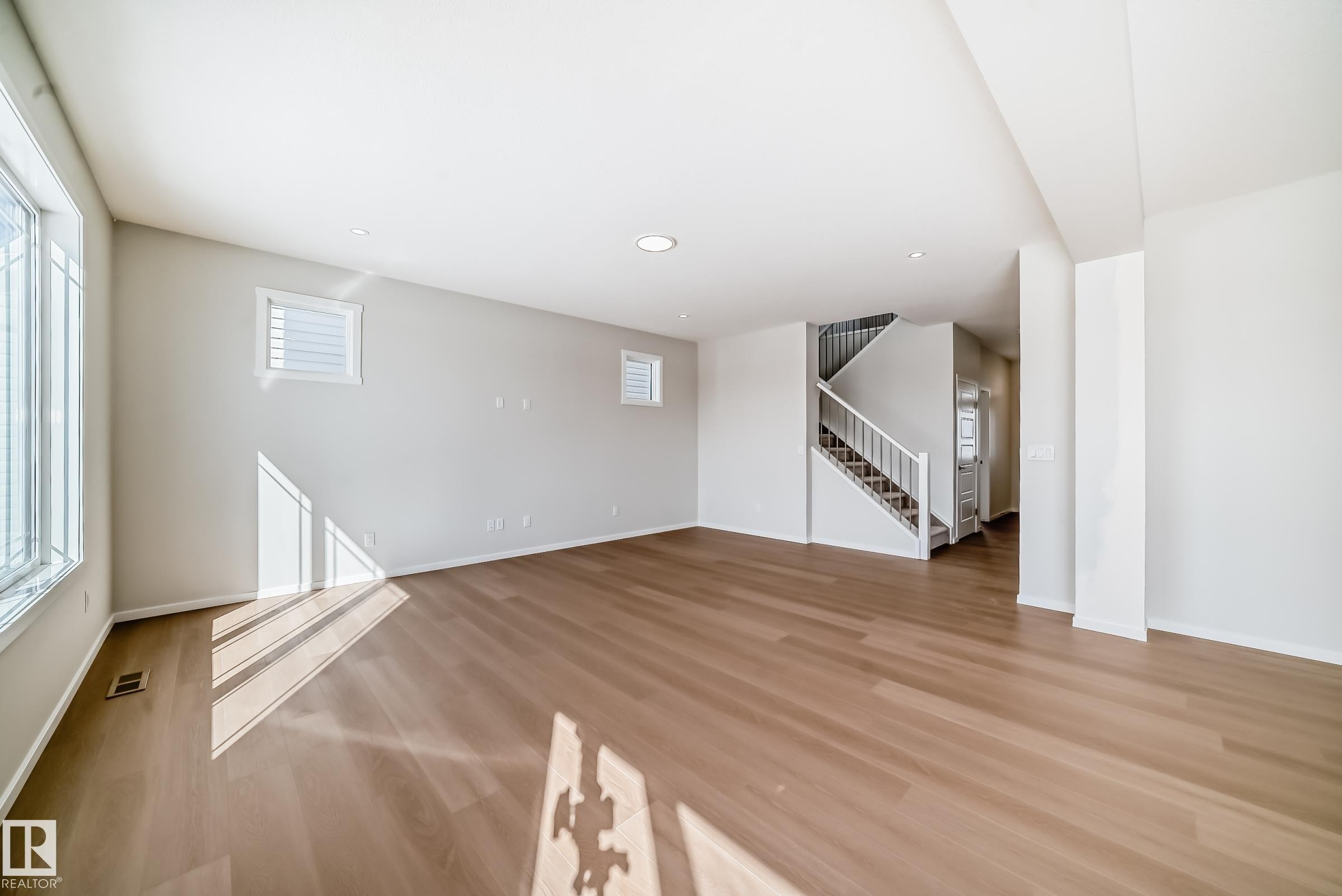 Expansive main living area featuring light wood flooring, several windows for natural illumination, and a staircase with white railings - 1516 206 Street Nw, Edmonton, AB - Indoor Photo Showing Other Room