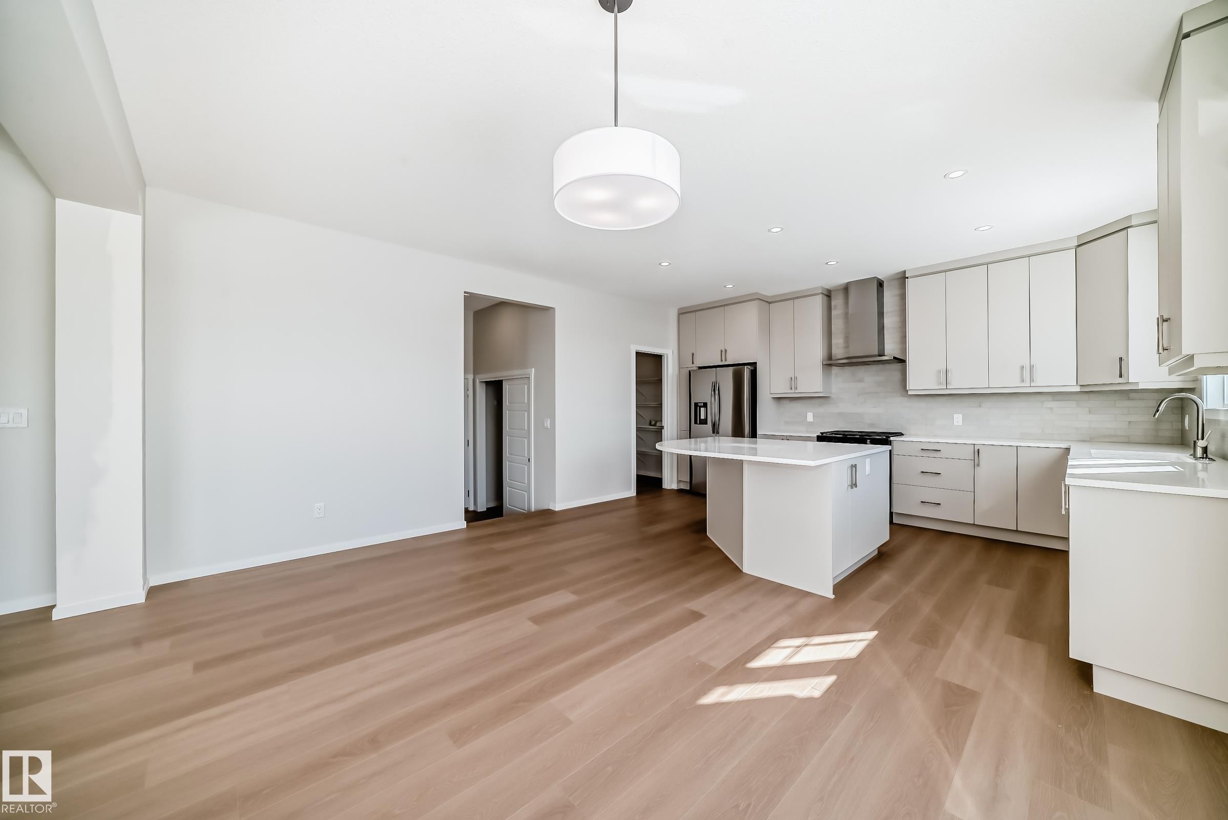 This open-concept kitchen features a large island with a white countertop, light-colored cabinetry, stainless steel appliances, and light wood flooring - 1516 206 Street Nw, Edmonton, AB - Indoor Photo Showing Kitchen