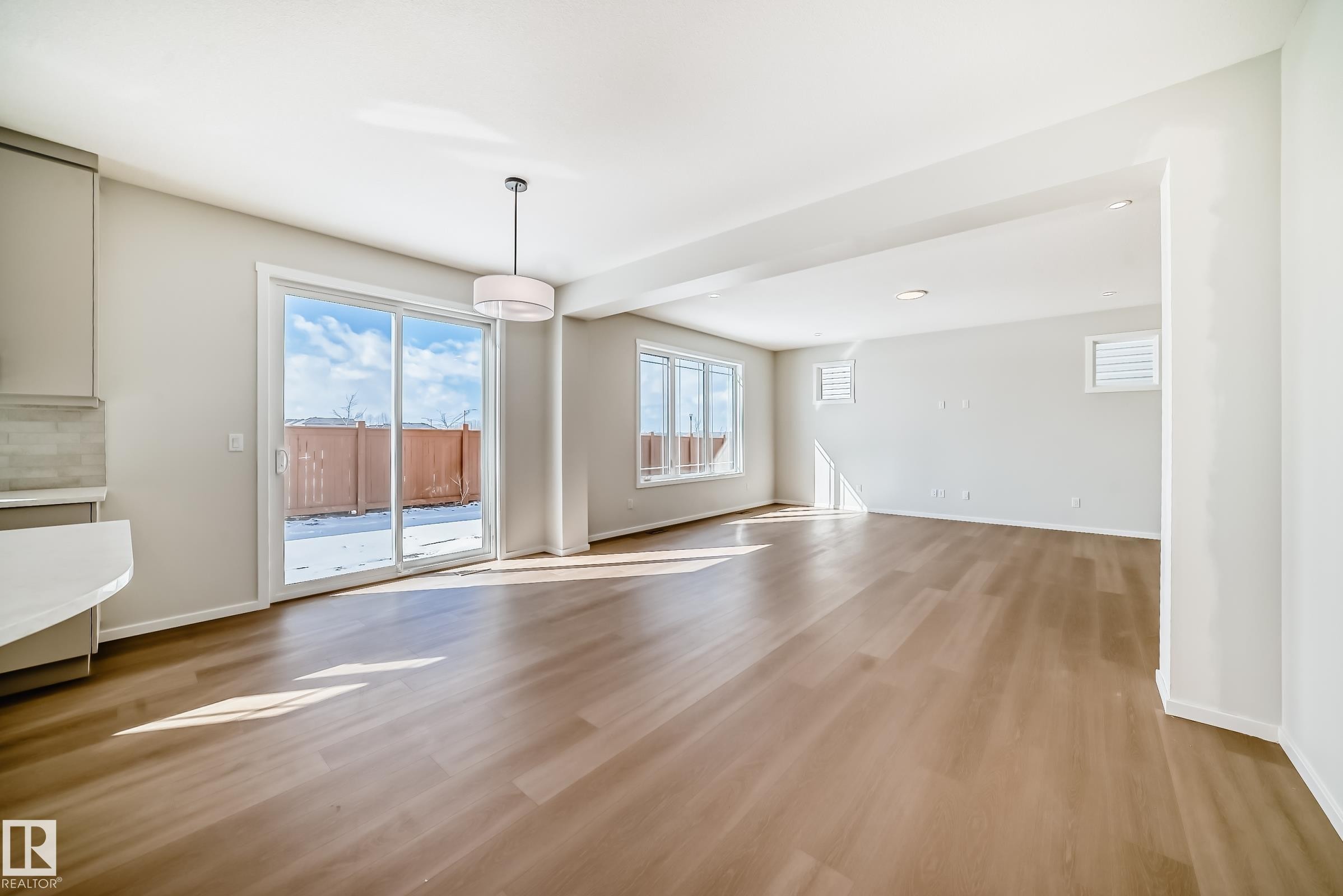 Spacious open concept living area featuring light wood flooring, recessed lighting, and large windows, including a sliding glass door - 1516 206 Street Nw, Edmonton, AB - Indoor