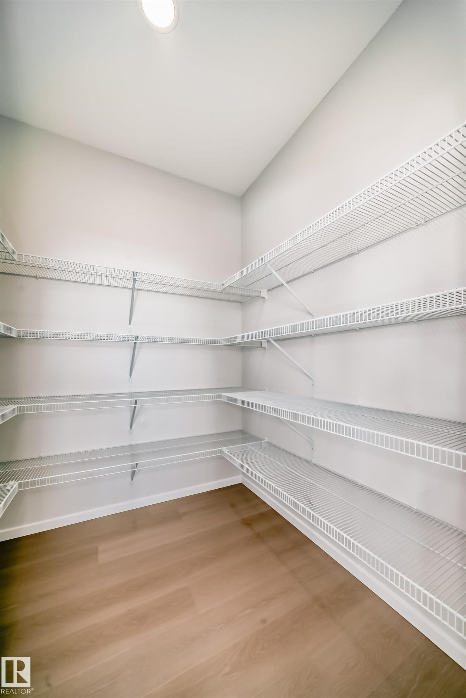 Spacious walk-in pantry featuring light wood-style flooring, white wire shelving, and an overhead light fixture - 1516 206 Street Nw, Edmonton, AB - Indoor With Storage