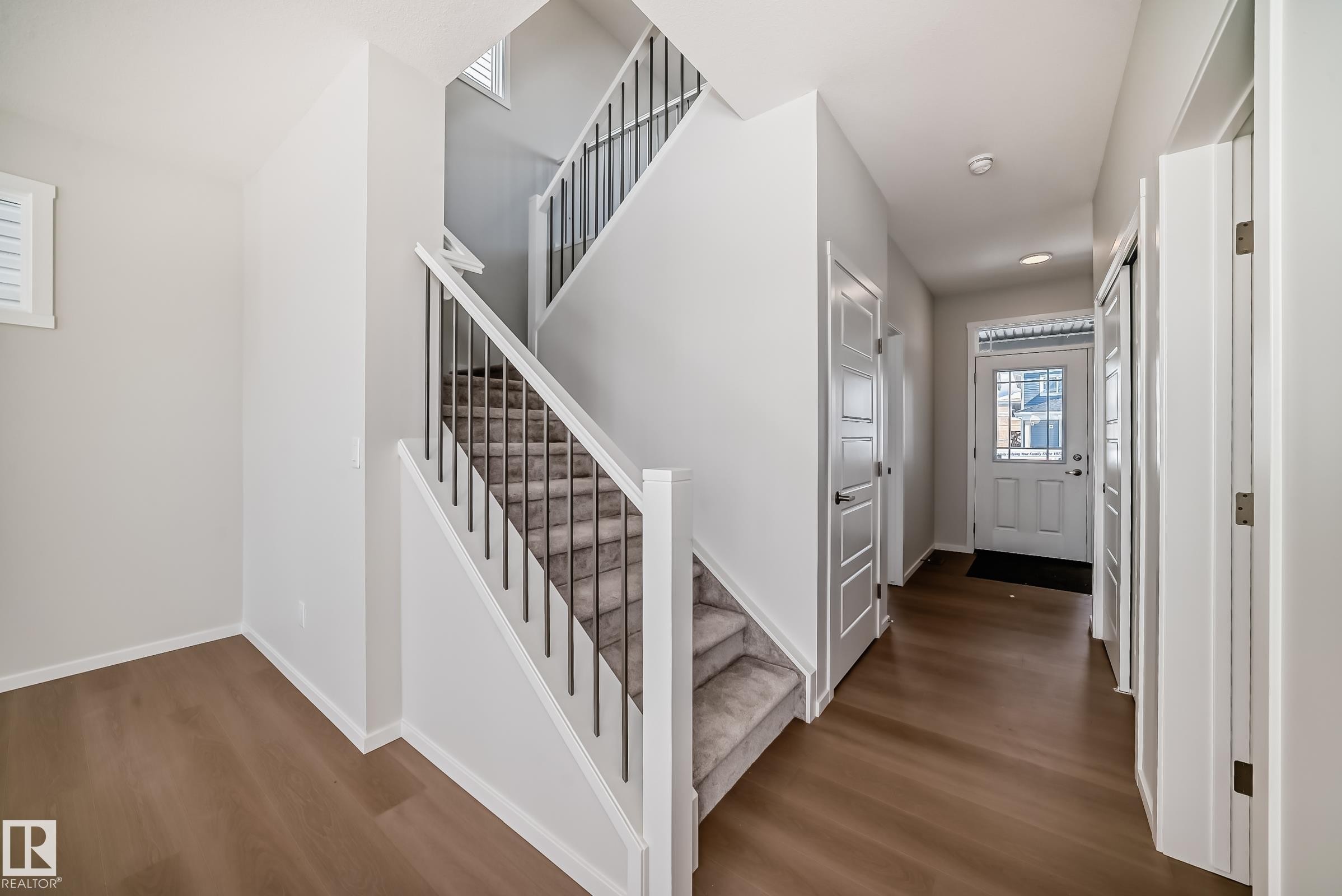 The property features a welcoming entryway with hardwood flooring and a carpeted staircase with white risers and dark balusters - 1516 206 Street Nw, Edmonton, AB - Indoor Photo Showing Other Room