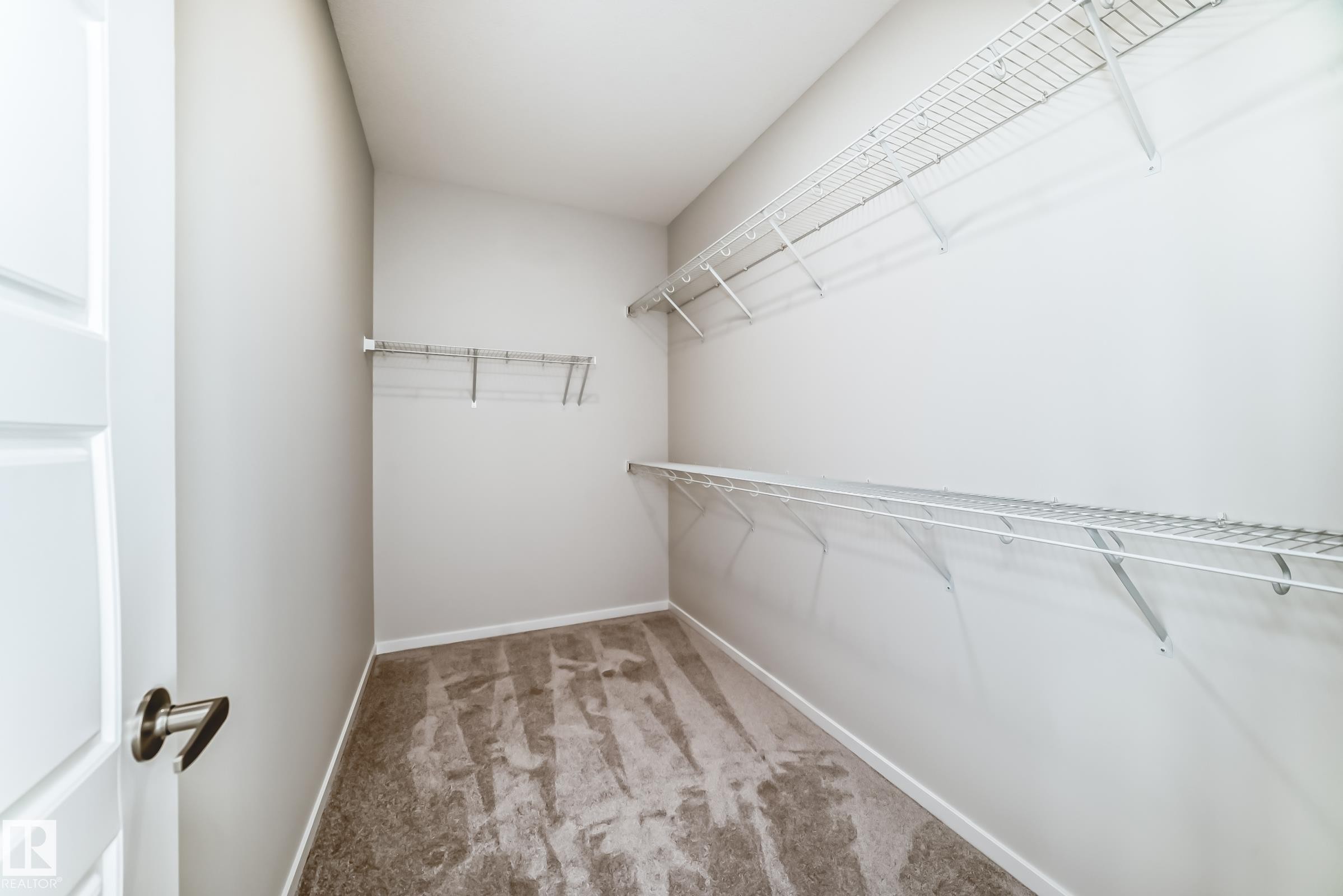 This spacious closet features neutral-toned carpet, light gray walls, and white wire shelving for storage - 1516 206 Street Nw, Edmonton, AB - Indoor With Storage