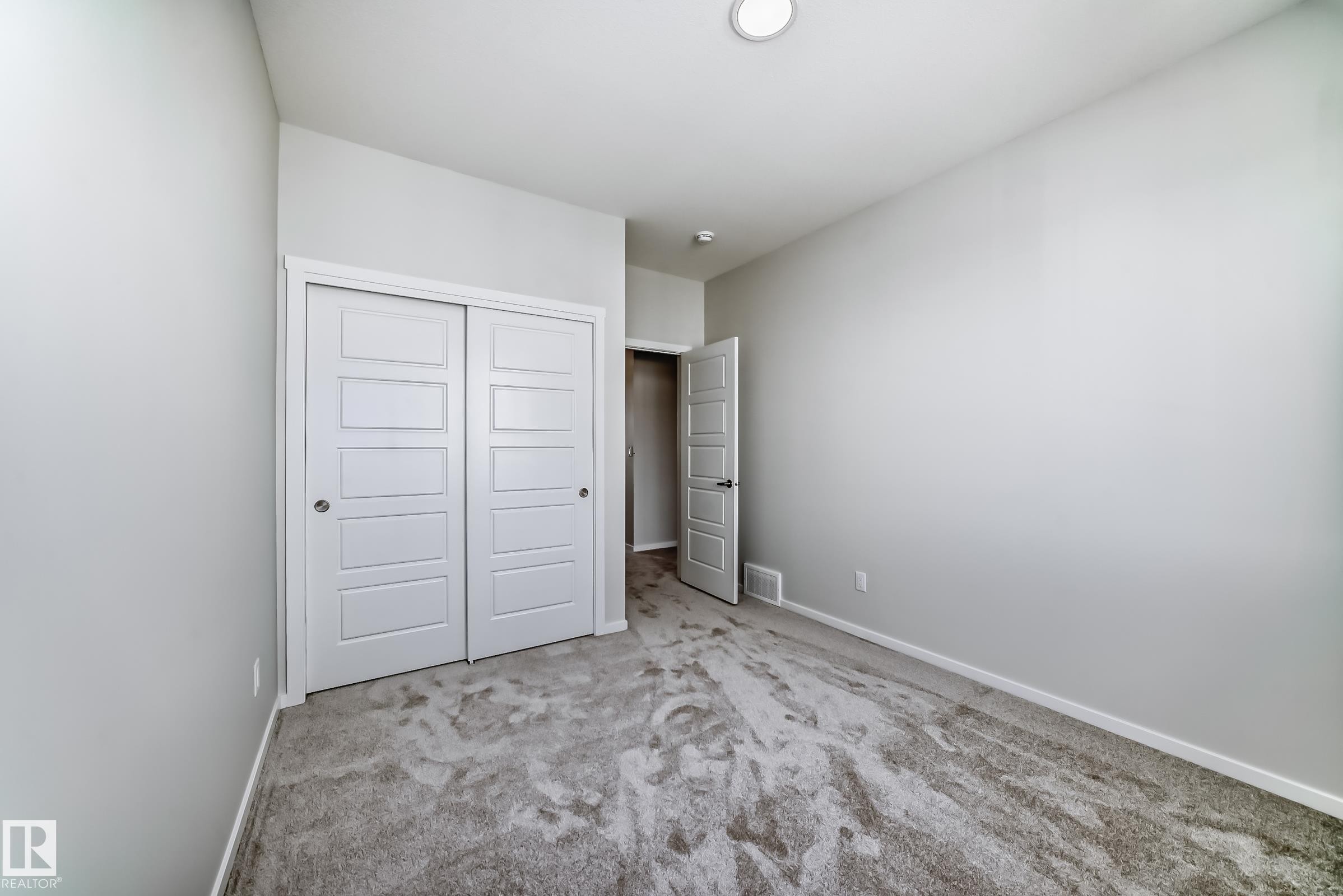 Bedroom featuring light gray walls, gray carpet, white trim, and a white sliding closet door - 1516 206 Street Nw, Edmonton, AB - Indoor Photo Showing Other Room