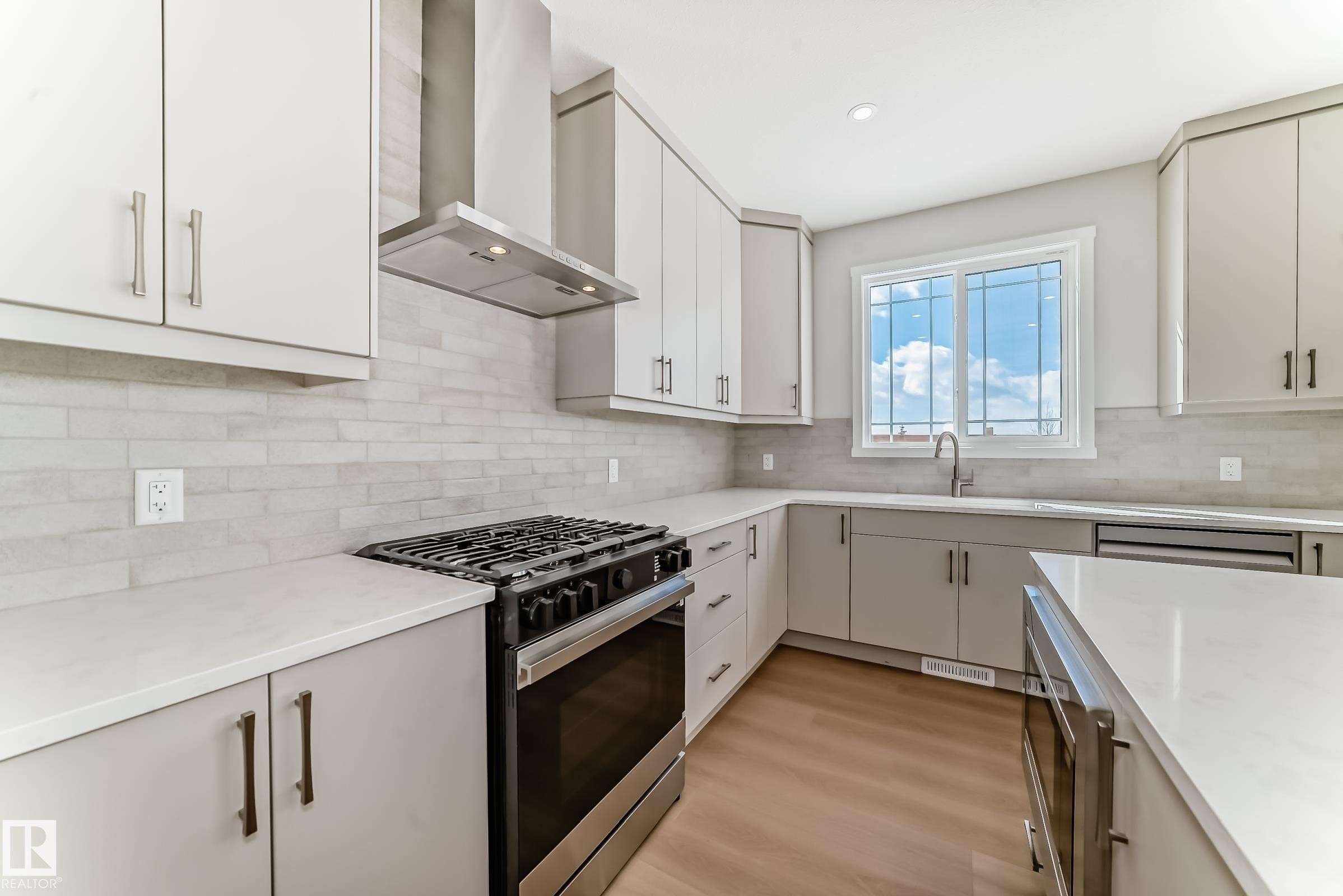 The kitchen features extensive white countertops, light-colored cabinetry, and a gas range with an overhead stainless steel exhaust hood - 1516 206 Street Nw, Edmonton, AB - Indoor Photo Showing Kitchen With Upgraded Kitchen