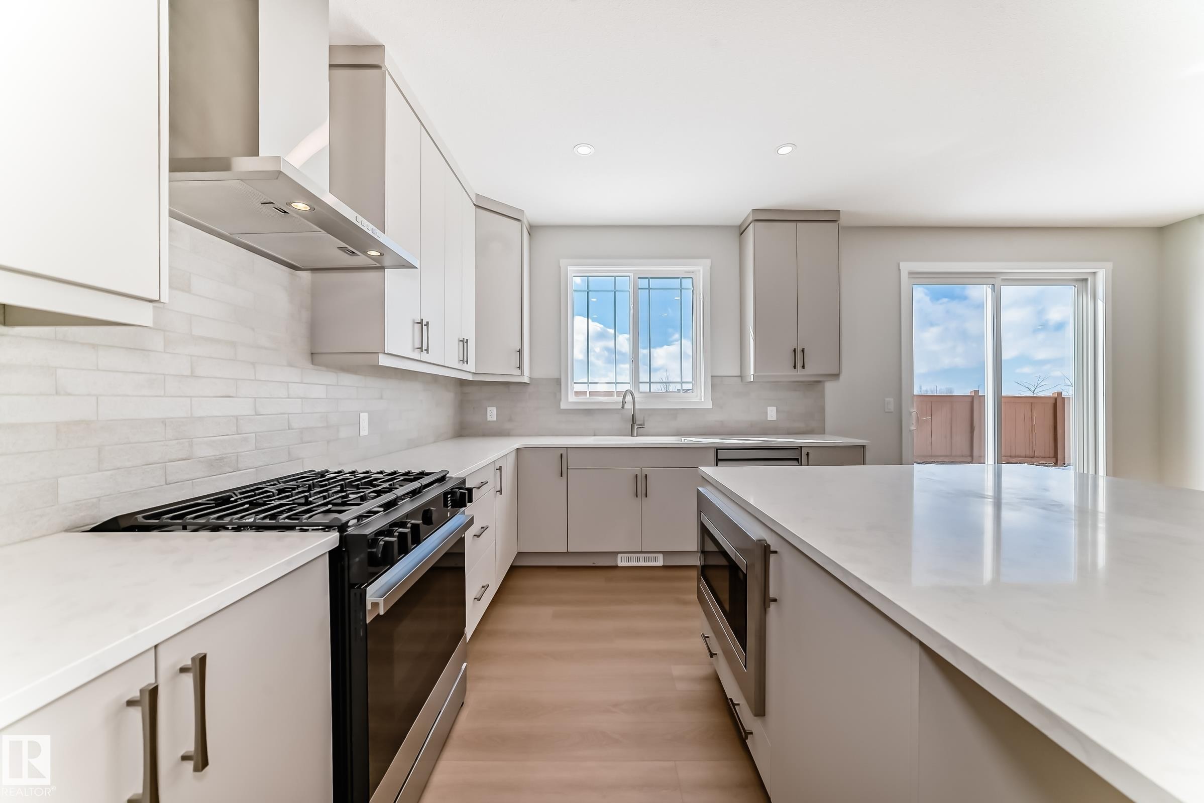 Modern kitchen featuring light cabinetry, a gas range with a stainless steel hood, light countertops, and a sliding glass door - 1516 206 Street Nw, Edmonton, AB - Indoor Photo Showing Kitchen With Upgraded Kitchen