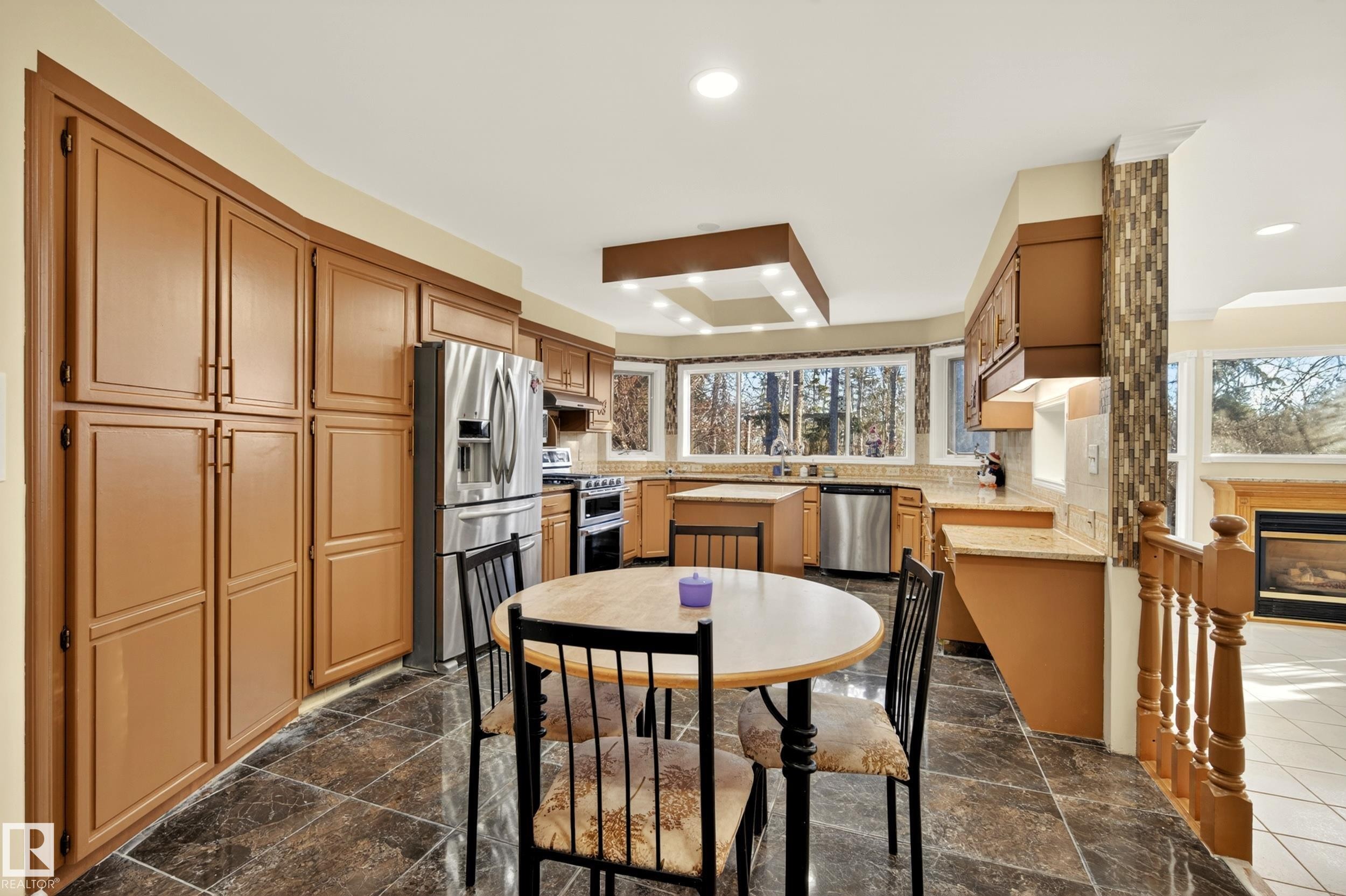 Kitchen featuring extensive cabinetry, stainless steel appliances, dark stone-finish tile flooring, recessed lighting, and a bay window overlooking exterior trees - 33 Glen Meadow Crescent, St. Albert, AB - Indoor Photo Showing Other Room