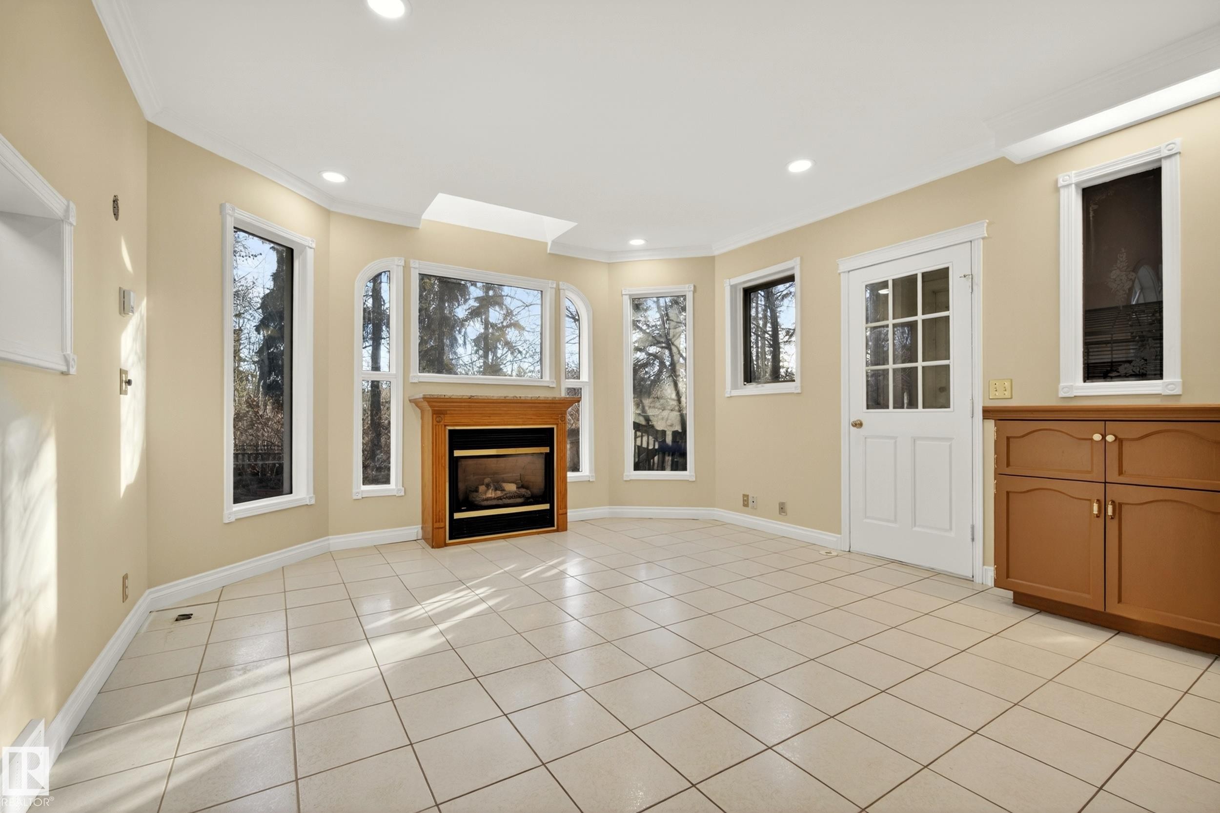 Spacious room featuring light-toned tile flooring and a gas fireplace with a wood-finish mantel and stone surround - 33 Glen Meadow Crescent, St. Albert, AB - Indoor With Fireplace