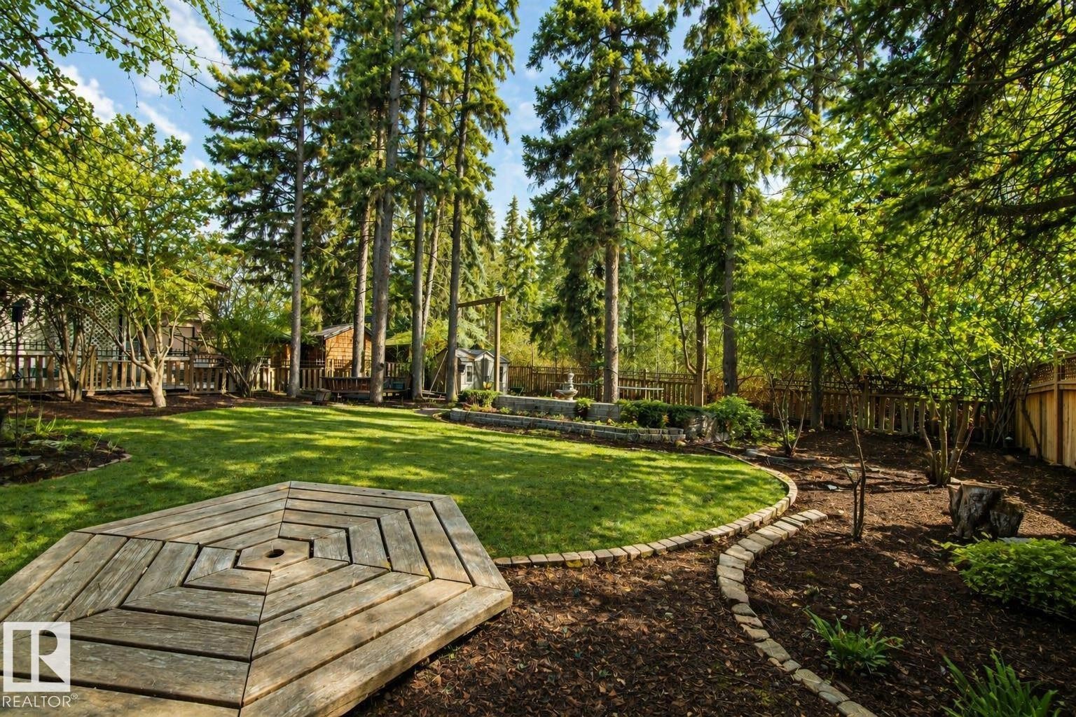 Expansive backyard featuring a central lawn, mature trees, a decorative wood-plank patio, and a sculpted stone-edged pathway - 33 Glen Meadow Crescent, St. Albert, AB - Outdoor