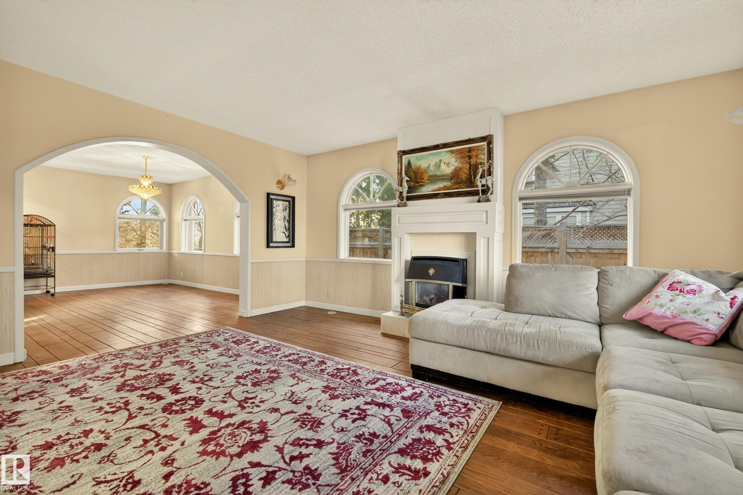 Living area featuring a fireplace with a mantel, arched windows, and wood-finish flooring - 33 Glen Meadow Crescent, St. Albert, AB - Indoor Photo Showing Living Room With Fireplace
