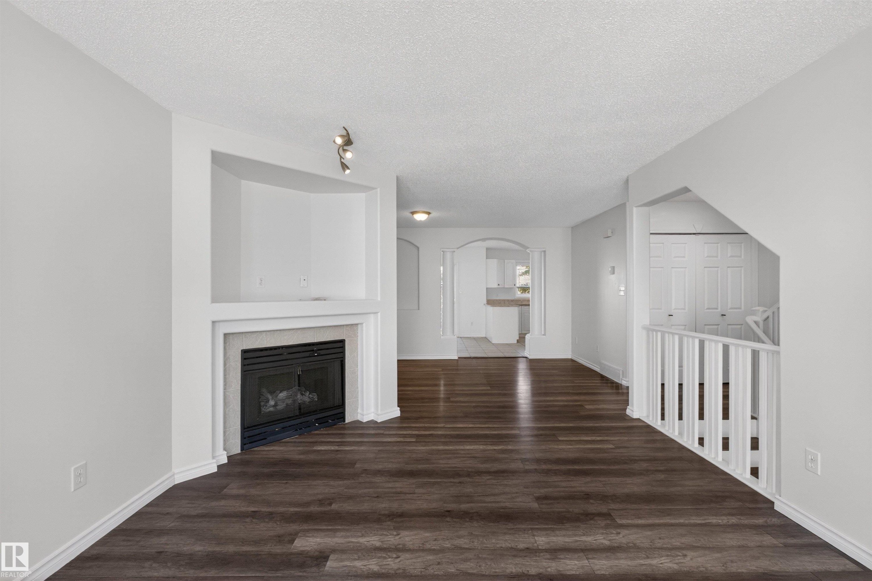 Living area featuring dark wood-finish flooring, a built-in fireplace with a hearth, white wall finishes, and a track lighting fixture - 6 1237 Carter Crest Road, Edmonton, AB