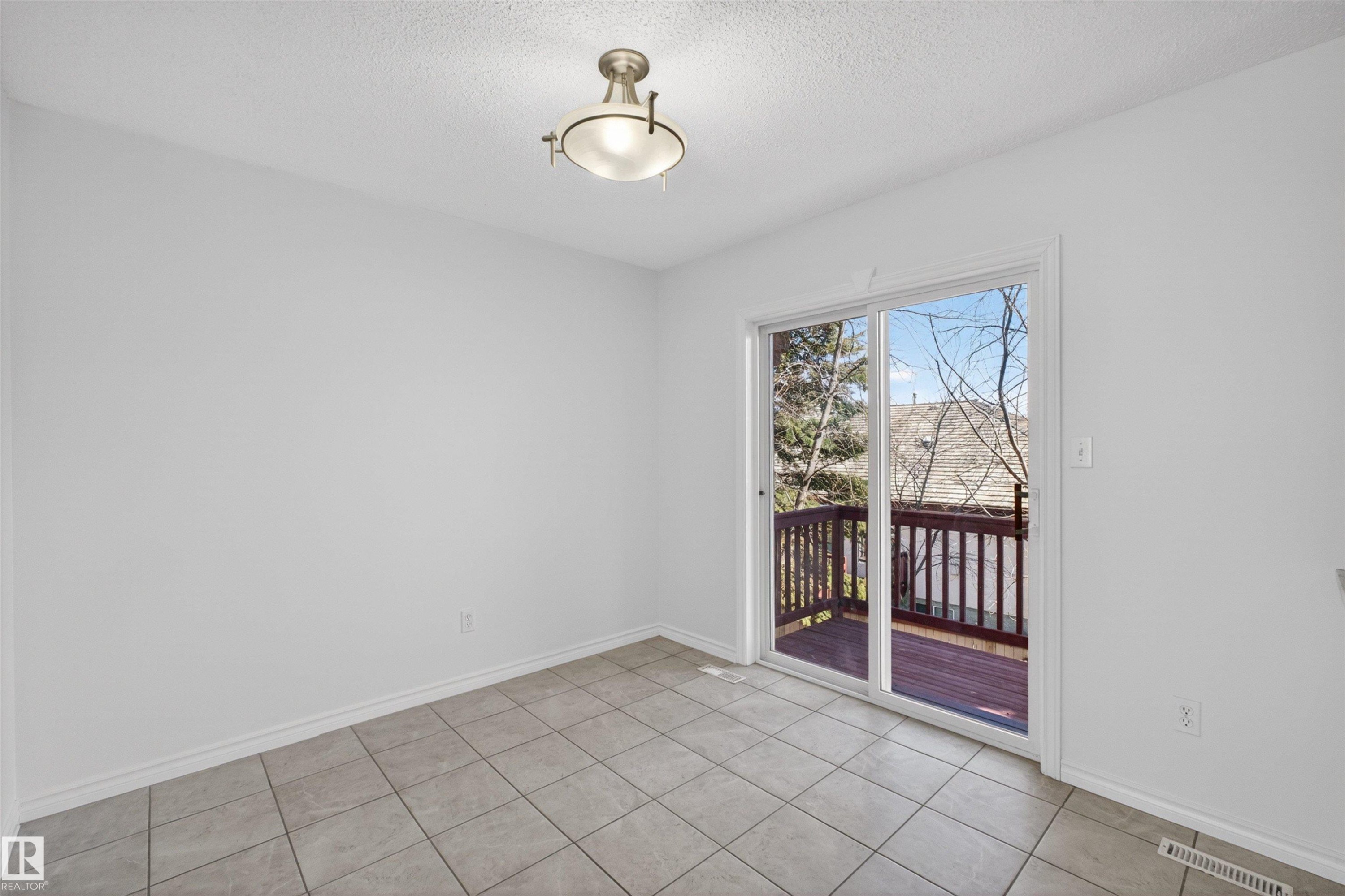 Room featuring neutral tile flooring, white baseboards, and a glass sliding door providing access to an exterior wood deck - 6 1237 Carter Crest Road, Edmonton, AB