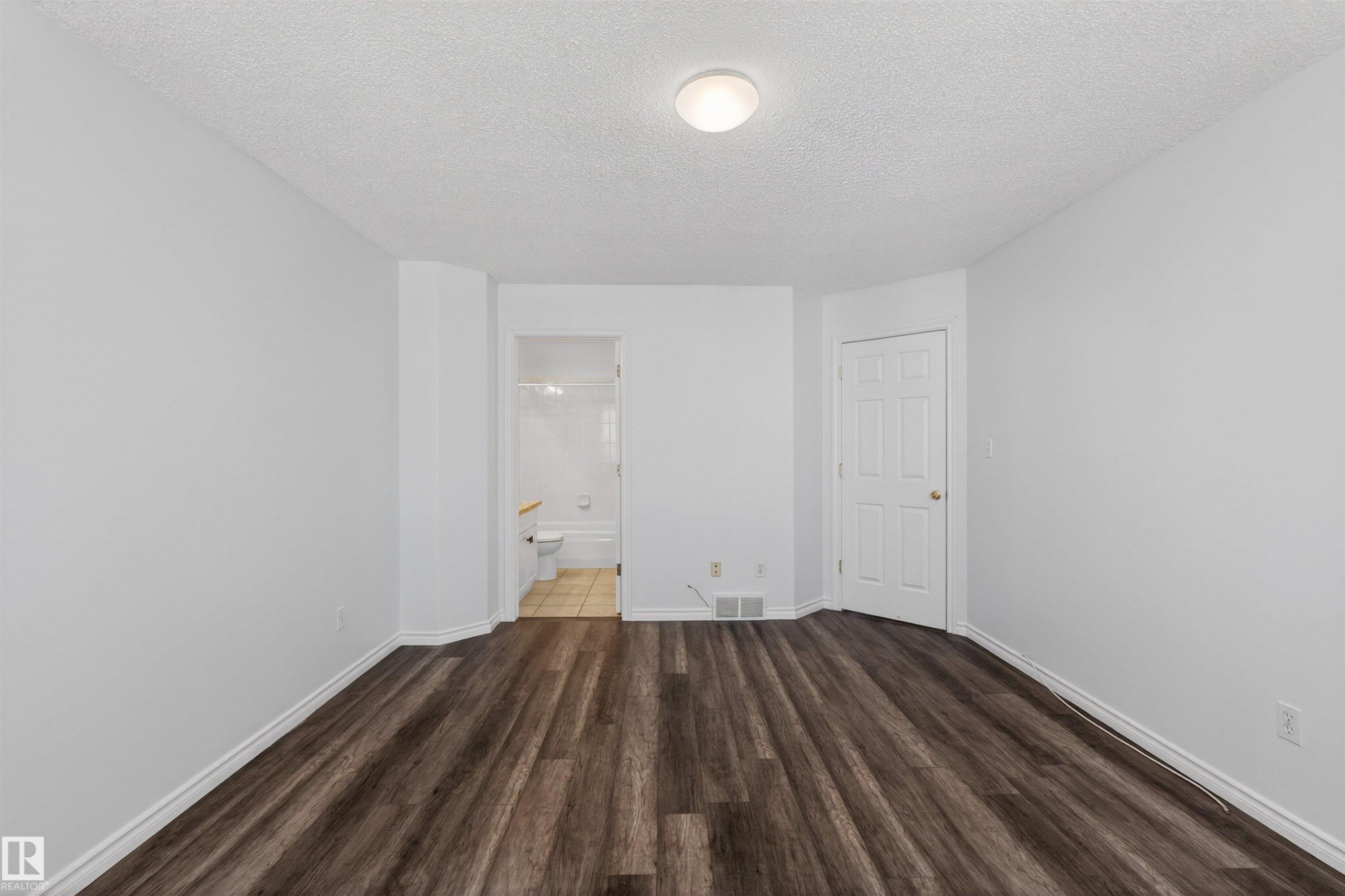 Spacious room featuring wood-finish flooring, white baseboards, and a neutral wall palette - 6 1237 Carter Crest Road, Edmonton, AB