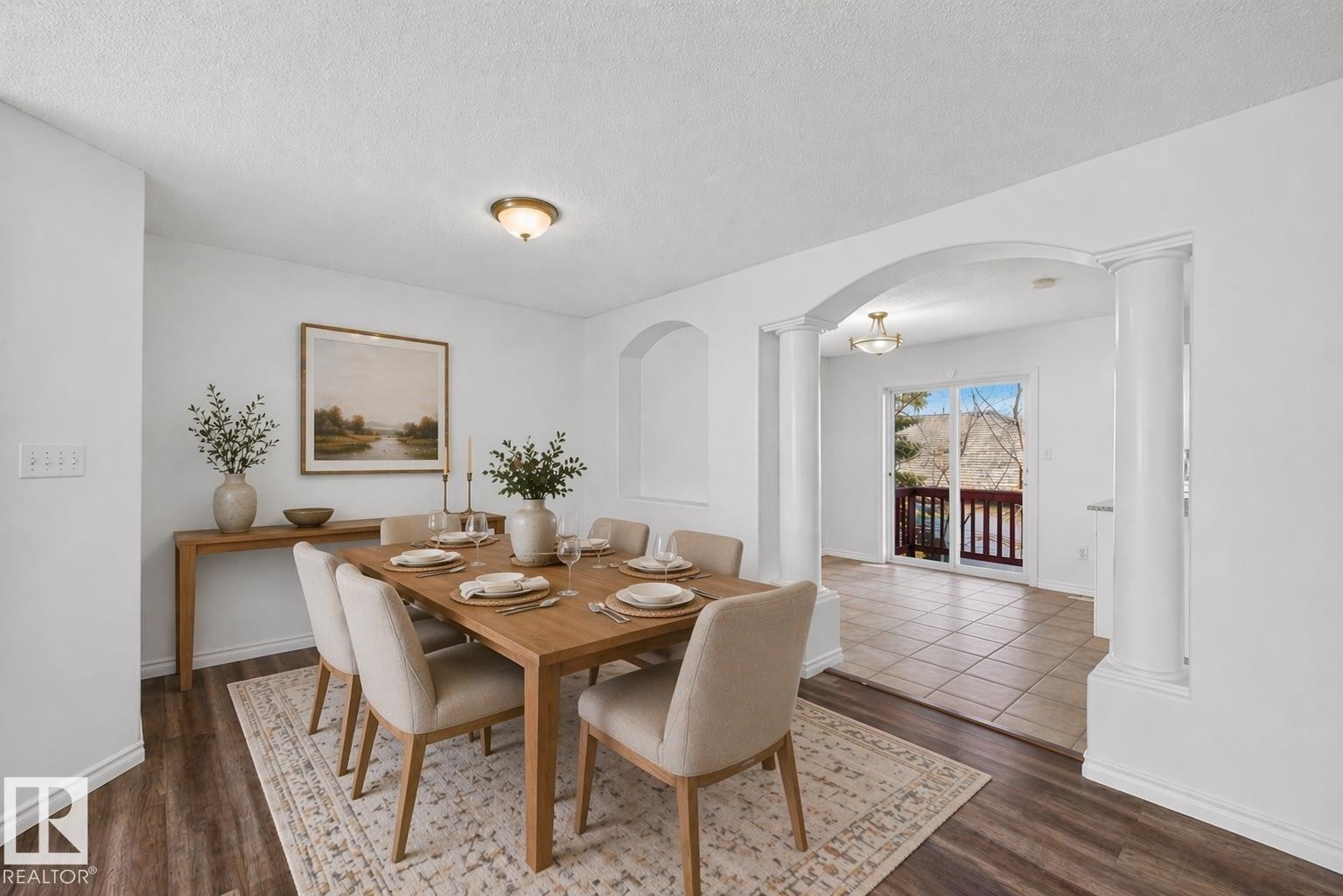 Formal dining area featuring wood-finish flooring, an arched entryway with columns, and an adjacent outdoor balcony with mountain scenery - 6 1237 Carter Crest Road, Edmonton, AB