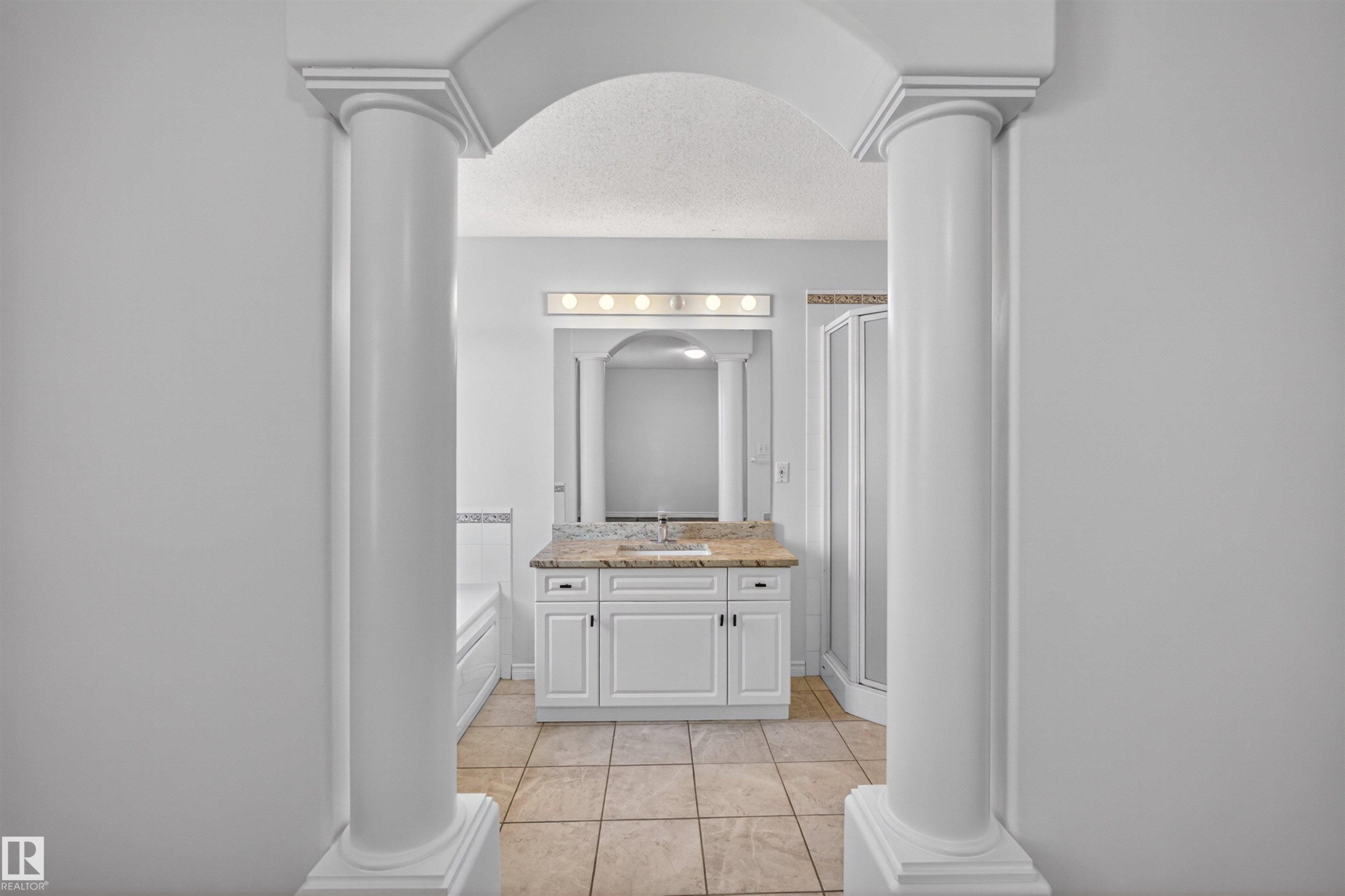 Arched entryway with columns framing a bathroom featuring a white vanity with a light-toned countertop, a frameless mirror, and a multi-bulb vanity light - 6 1237 Carter Crest Road, Edmonton, AB