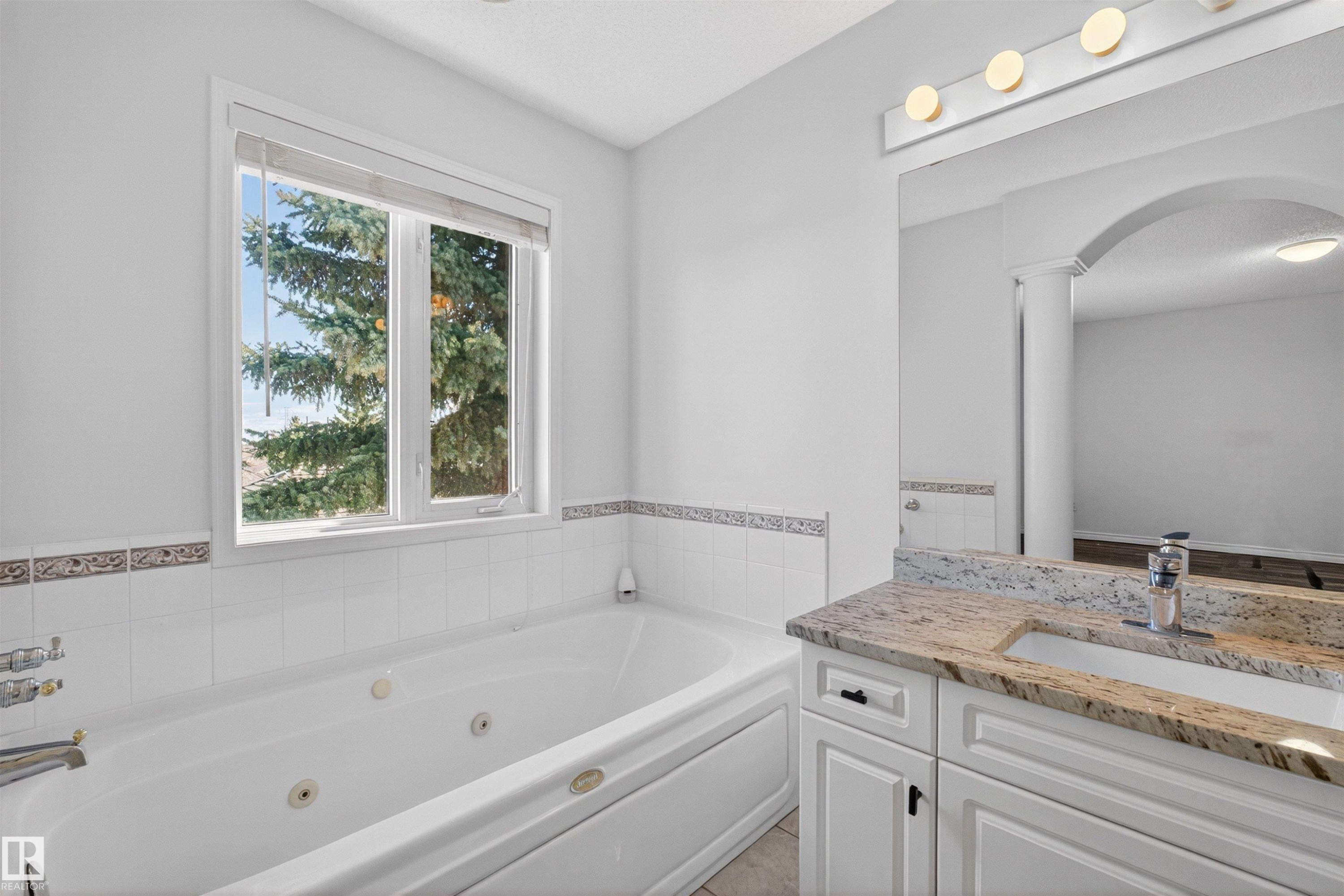 White jetted tub with tiled surround, dual windows, and decorative border tile - 6 1237 Carter Crest Road, Edmonton, AB
