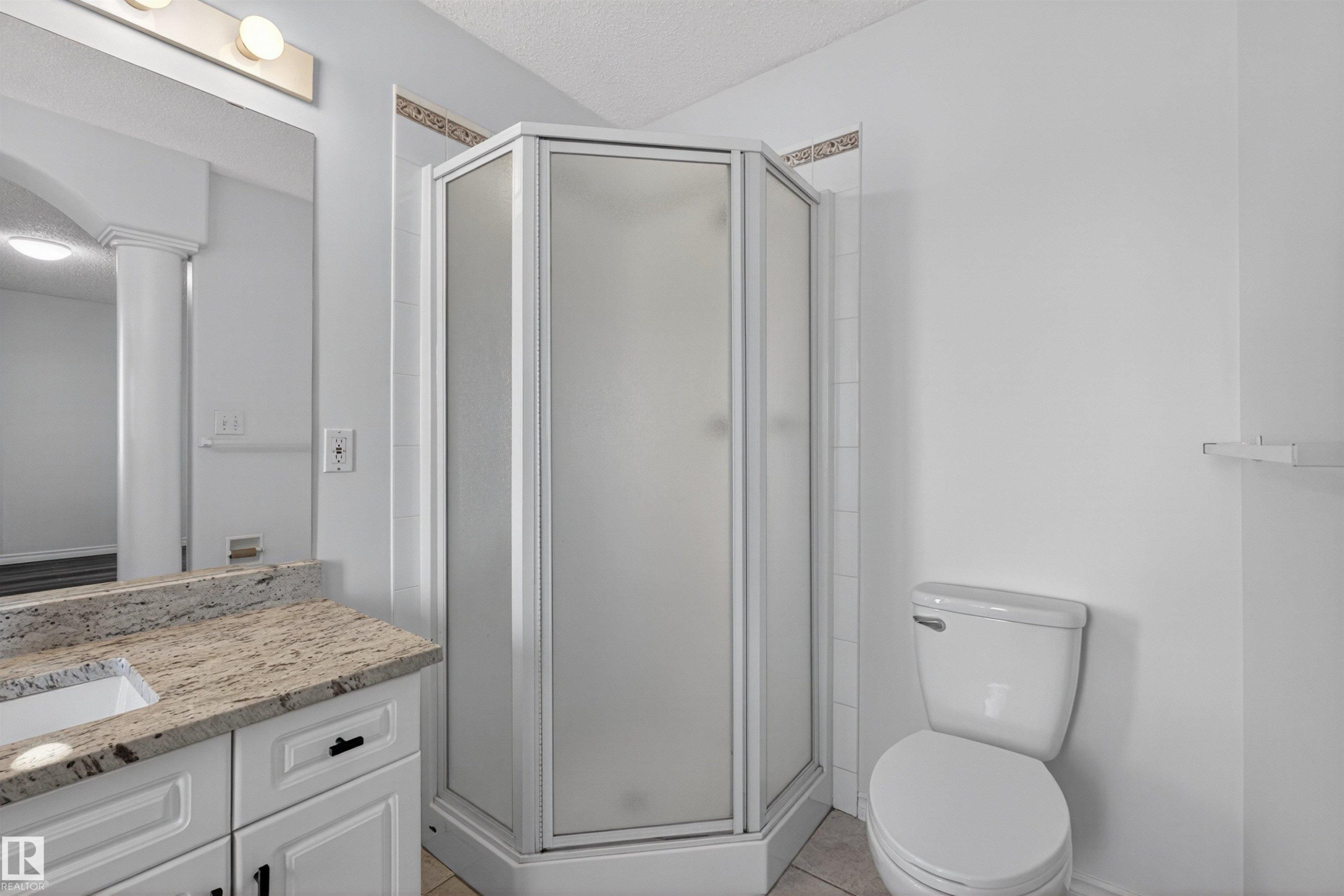 Bathroom featuring a corner shower enclosure, white vanity with a light-toned stone countertop, integrated sink, and white commode - 6 1237 Carter Crest Road, Edmonton, AB
