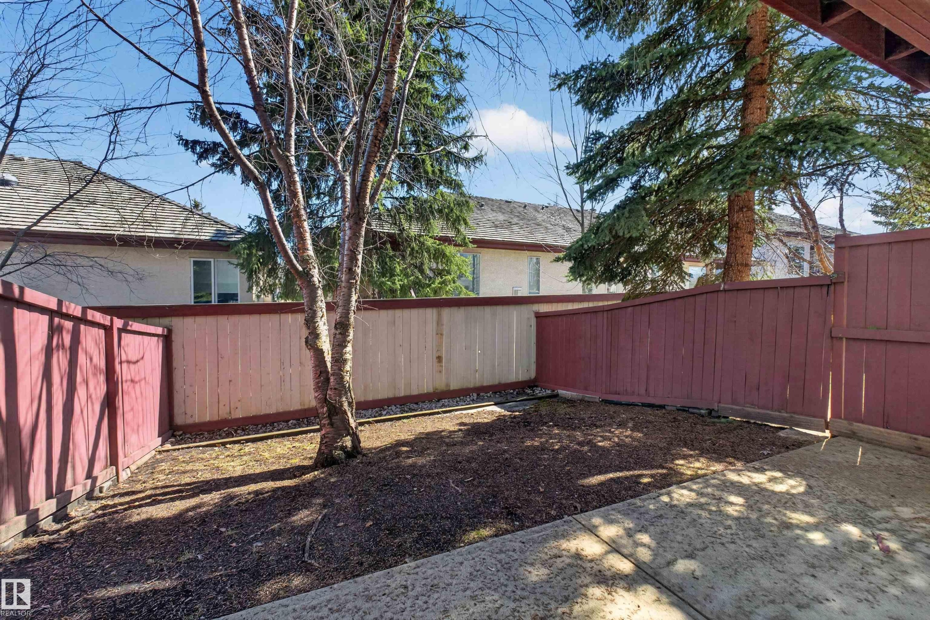 Fenced outdoor space featuring a concrete patio, a mature tree, and a blend of natural and painted wood fencing - 6 1237 Carter Crest Road, Edmonton, AB