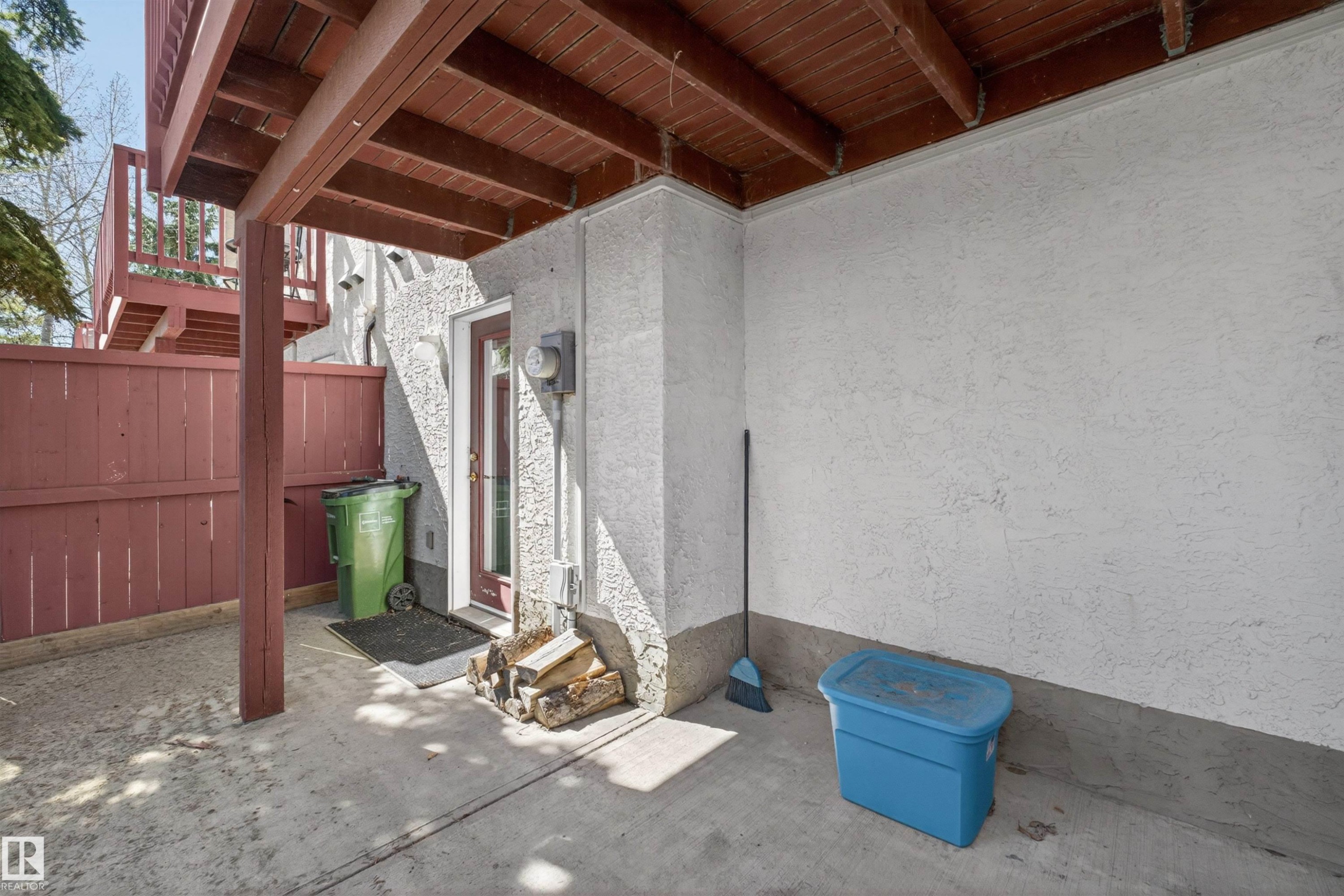 Covered concrete patio space featuring a stucco exterior wall and a red wood-paneled fence - 6 1237 Carter Crest Road, Edmonton, AB