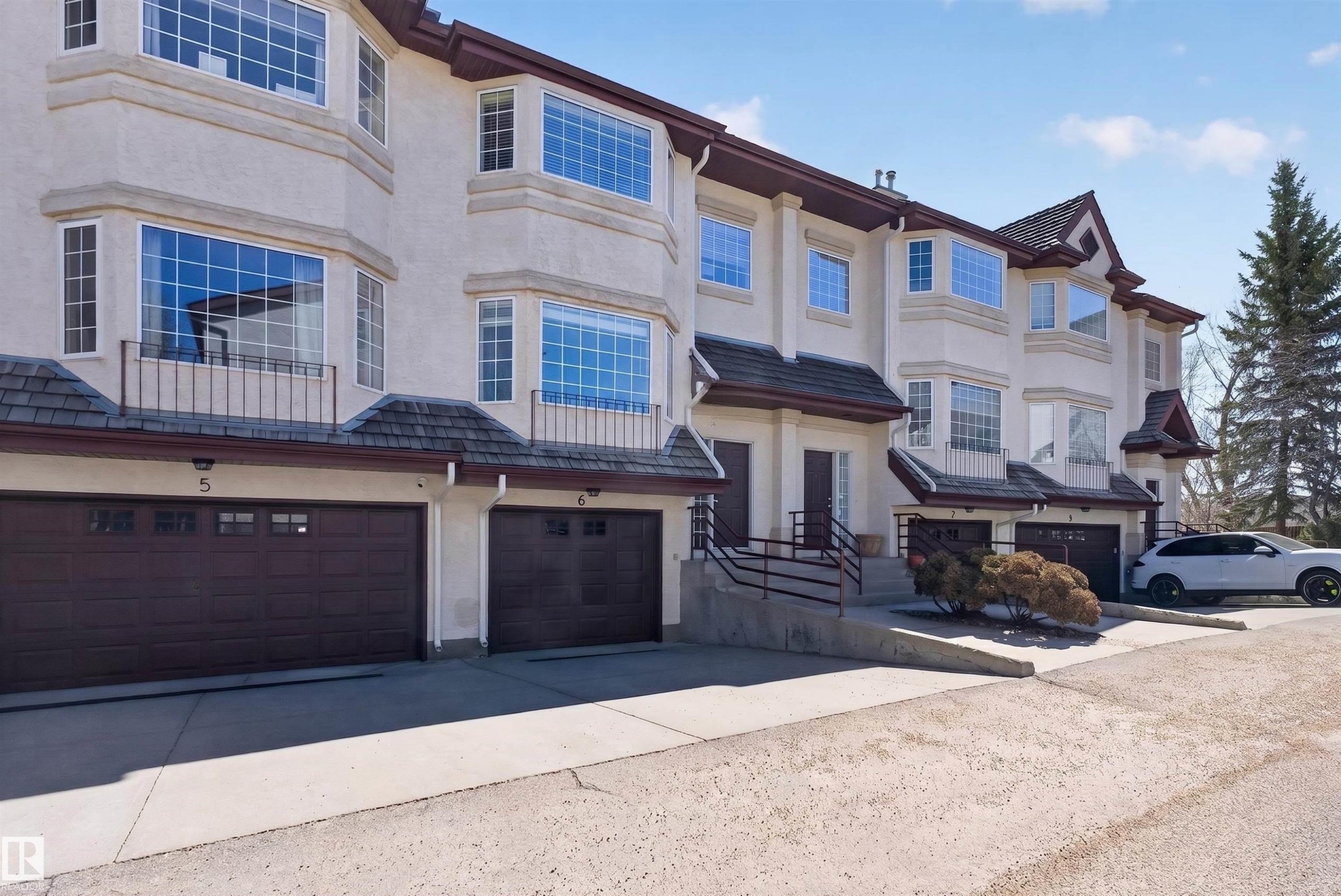 Multi-level townhome exterior featuring bay windows, individual garages with panel designs and transom windows, and a combination of stucco and shingle siding - 6 1237 Carter Crest Road, Edmonton, AB