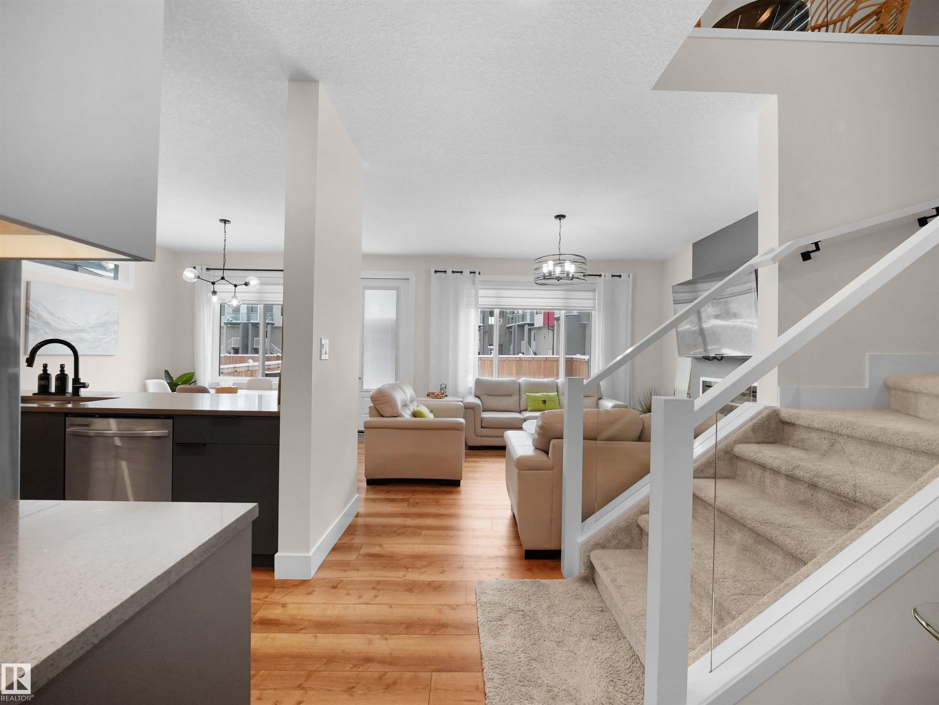 Open-concept living area featuring wood-finish flooring, a contemporary staircase with glass railing, and a kitchen island with stone countertop - 20827 130 Avenue Nw, Edmonton, AB - Indoor Photo Showing Kitchen