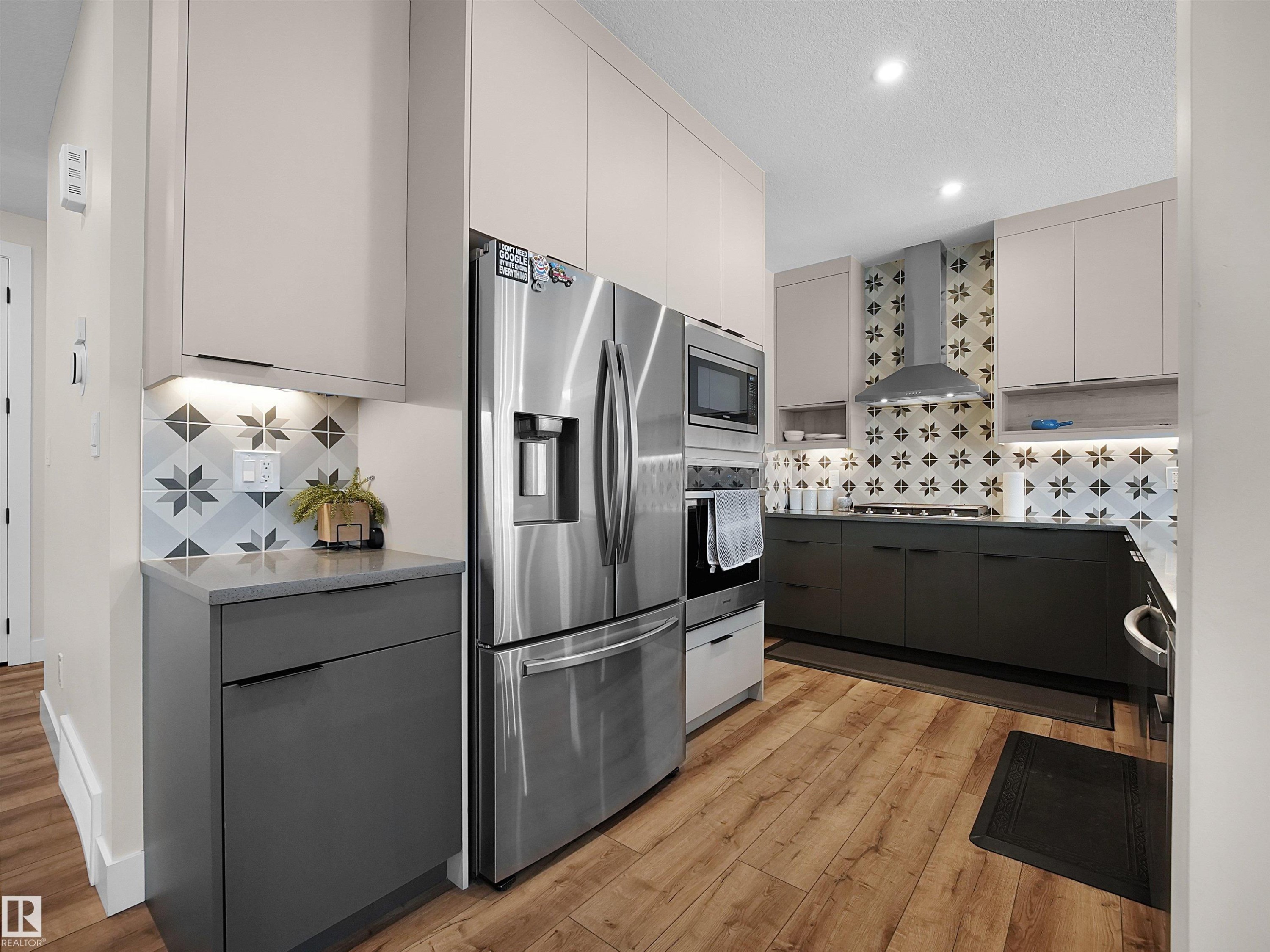 Modern kitchen featuring stainless steel appliances, two-tone cabinetry, wood-finish flooring, patterned tile backsplash, and recessed ceiling lighting - 20827 130 Avenue Nw, Edmonton, AB - Indoor Photo Showing Kitchen With Upgraded Kitchen