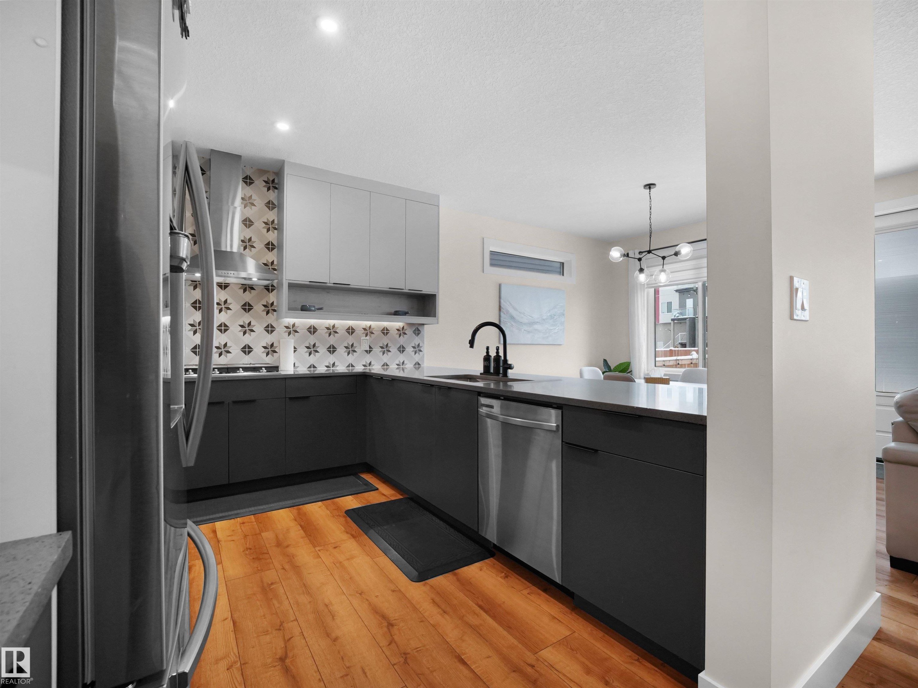 Modern kitchen featuring wood-finish flooring, two-tone cabinetry, stainless steel appliances, a decorative tile backsplash, and recessed lighting - 20827 130 Avenue Nw, Edmonton, AB - Indoor Photo Showing Kitchen With Upgraded Kitchen