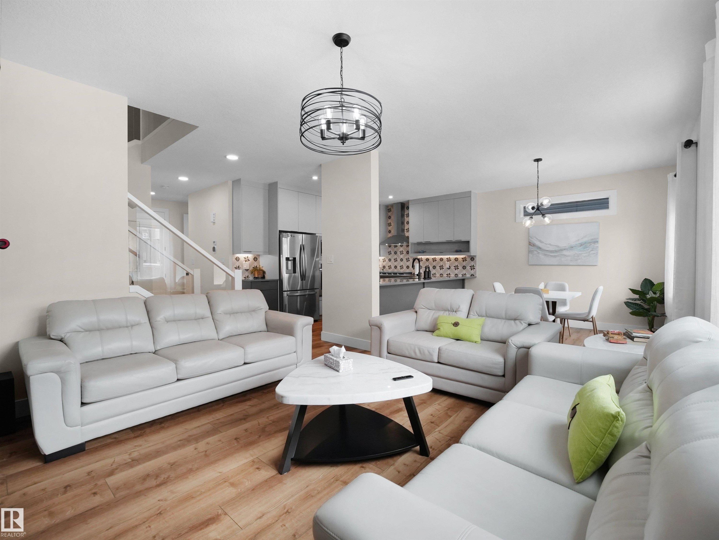 Open-concept living space featuring wood-finish flooring, recessed lighting, and a contemporary chandelier - 20827 130 Avenue Nw, Edmonton, AB - Indoor Photo Showing Living Room