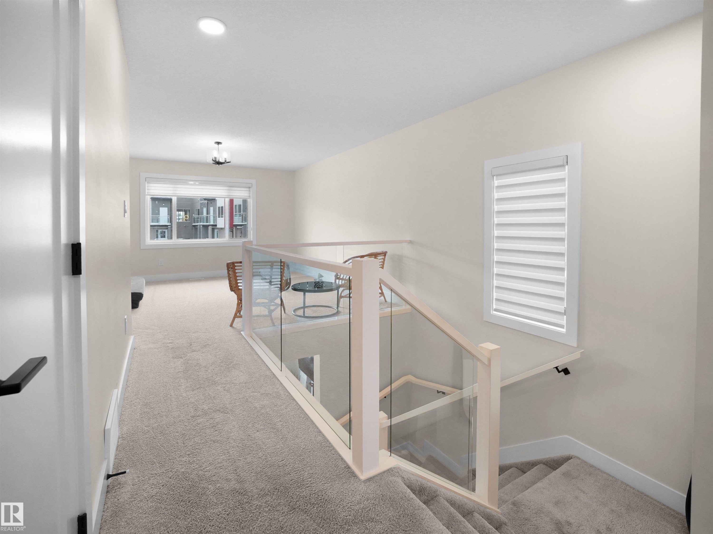 Carpeted upper-level landing featuring a contemporary glass and wood railing system, a recessed lighting fixture, and a window with blinds - 20827 130 Avenue Nw, Edmonton, AB - Indoor Photo Showing Other Room