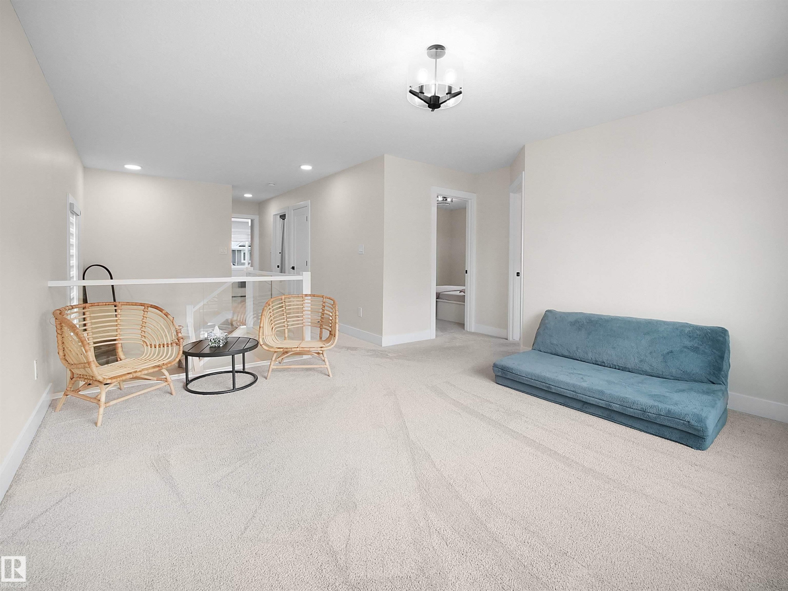 Spacious carpeted room featuring a modern ceiling light fixture, neutral wall paint, white baseboards, and a contemporary glass railing - 20827 130 Avenue Nw, Edmonton, AB - Indoor Photo Showing Other Room