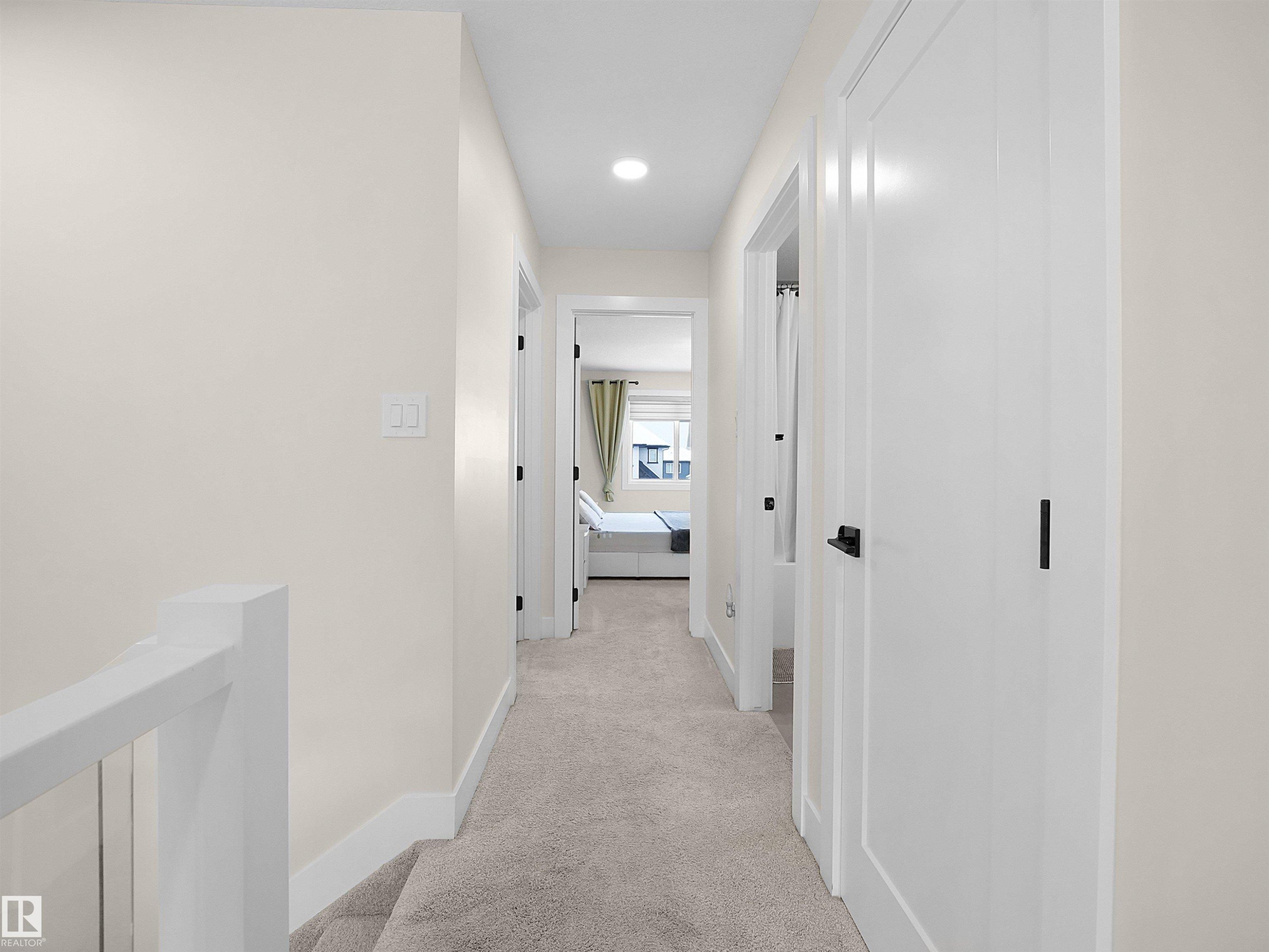 Carpeted hallway featuring white walls, contemporary recessed lighting, white doors with matte black hardware, and a white stair railing with thin balusters - 20827 130 Avenue Nw, Edmonton, AB - Indoor Photo Showing Other Room