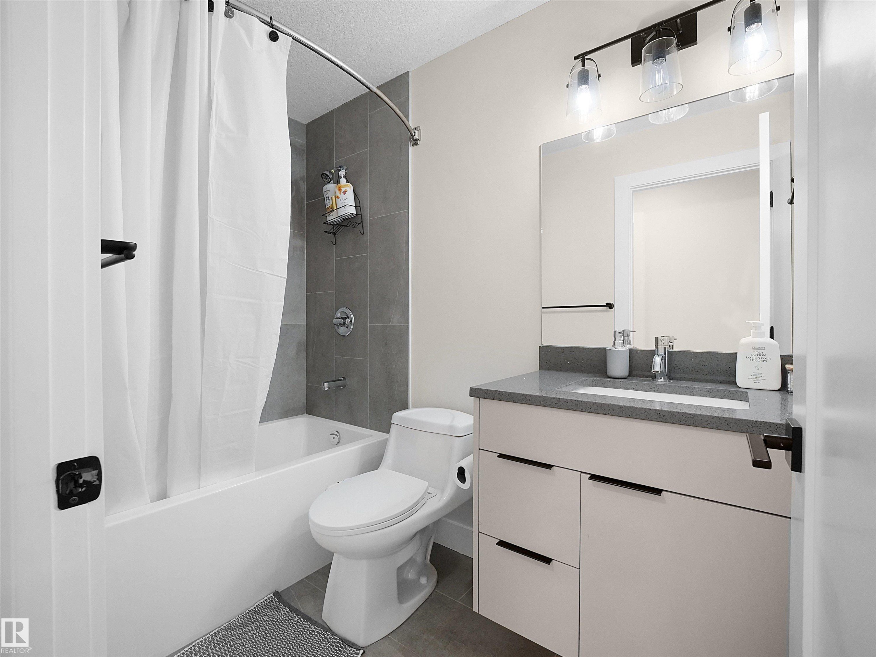 Full bathroom featuring a tub/shower combination with gray tile surround, a modern vanity with integrated sink and dark countertop, and matte black hardware - 20827 130 Avenue Nw, Edmonton, AB - Indoor Photo Showing Bathroom