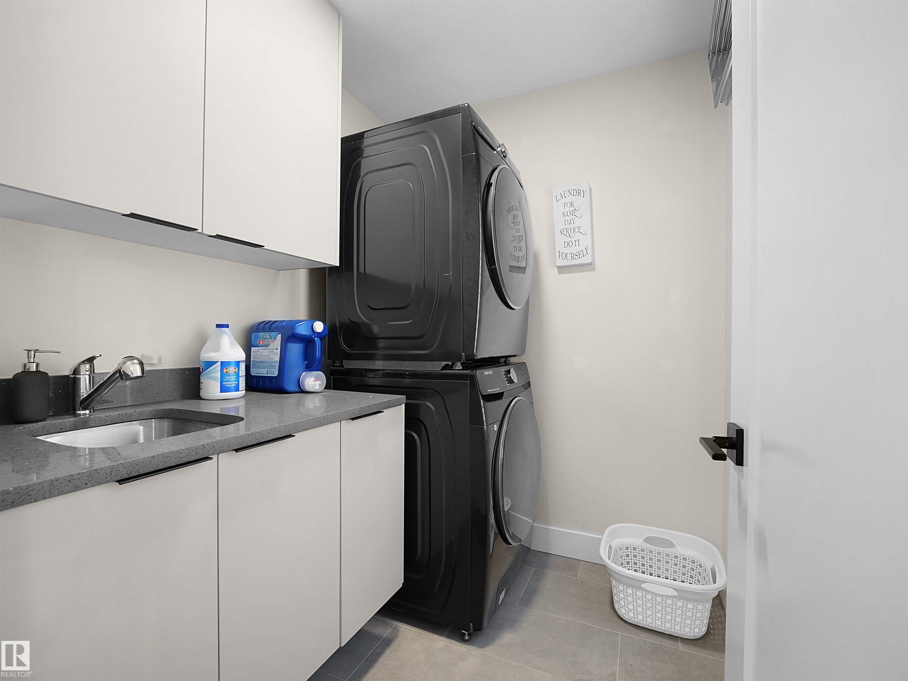Dedicated laundry area featuring a stacked appliance set, white cabinetry, a countertop with an integrated sink, and tile flooring - 20827 130 Avenue Nw, Edmonton, AB - Indoor Photo Showing Laundry Room