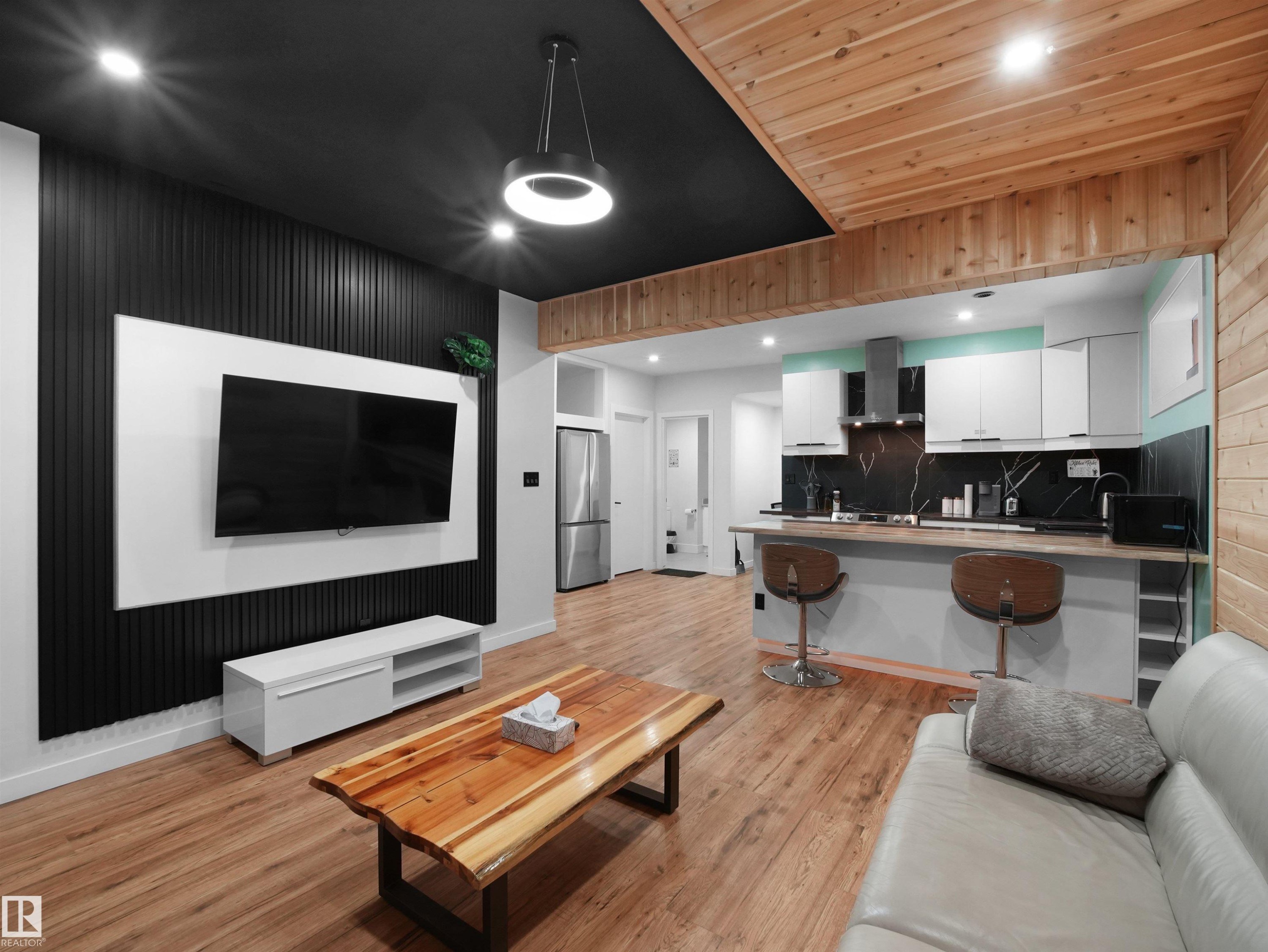 Open-concept living space featuring wood-finish flooring, a contemporary black slat accent wall, and a unique wood plank ceiling - 20827 130 Avenue Nw, Edmonton, AB - Indoor Photo Showing Living Room