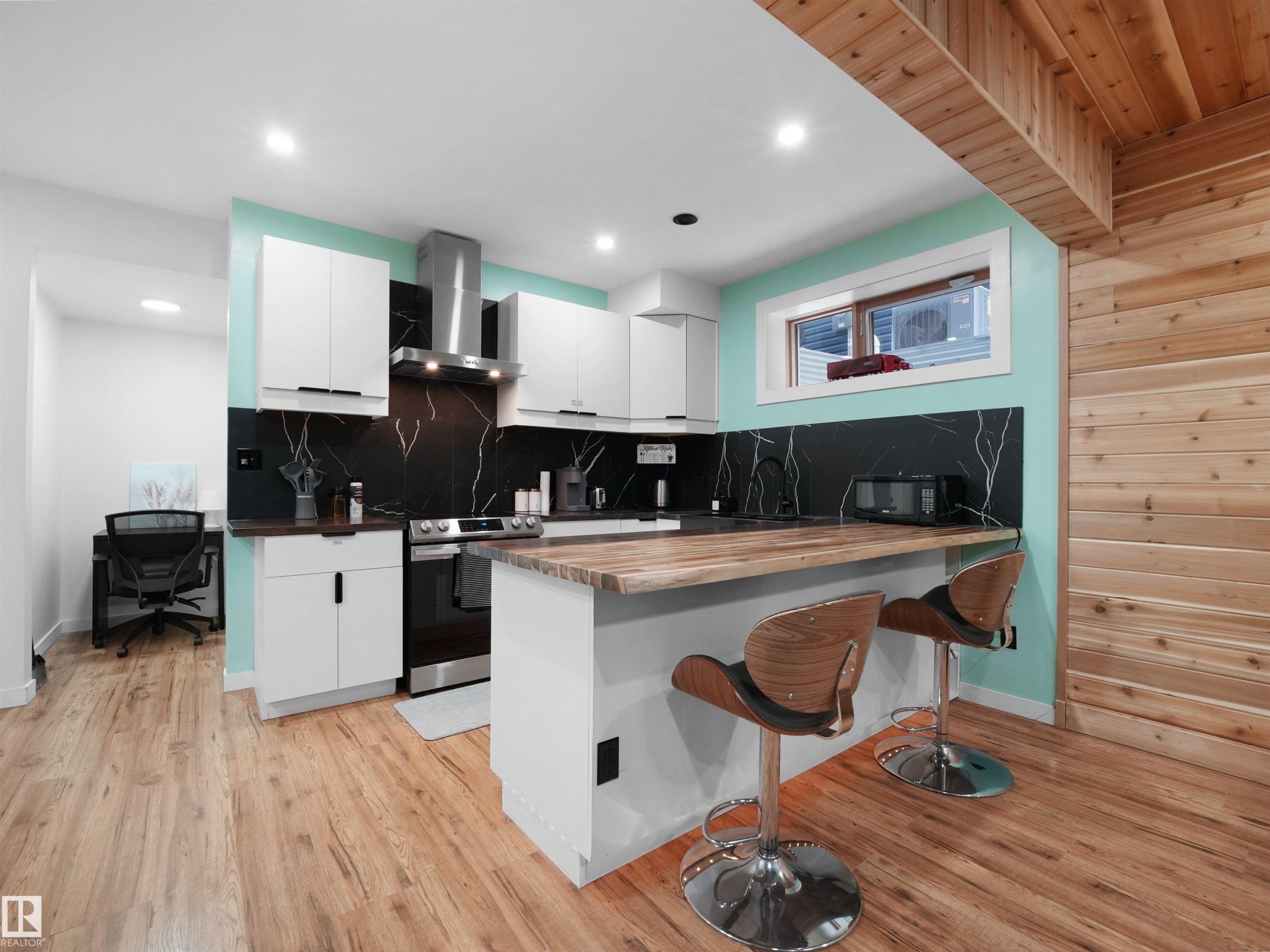 Contemporary kitchen featuring white cabinetry, black marbled backsplash, stainless steel appliances, a wood-finish island countertop, and recessed lighting - 20827 130 Avenue Nw, Edmonton, AB - Indoor Photo Showing Kitchen