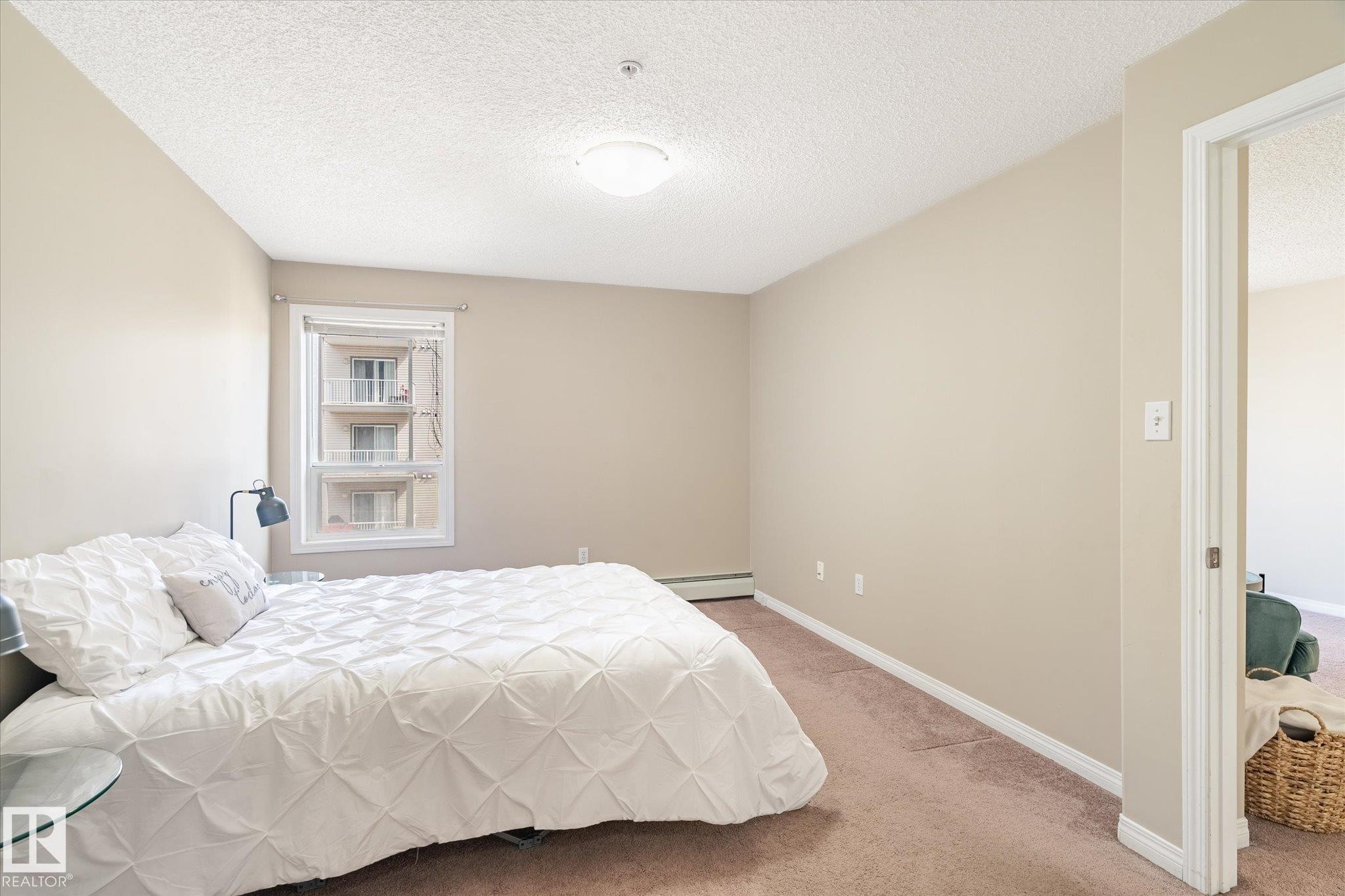 Bedroom featuring a window with white trim, beige wall paint, carpet flooring, a flush-mount ceiling light, and white baseboards - 203 155 Edwards Drive, Edmonton, AB - Indoor Photo Showing Bedroom