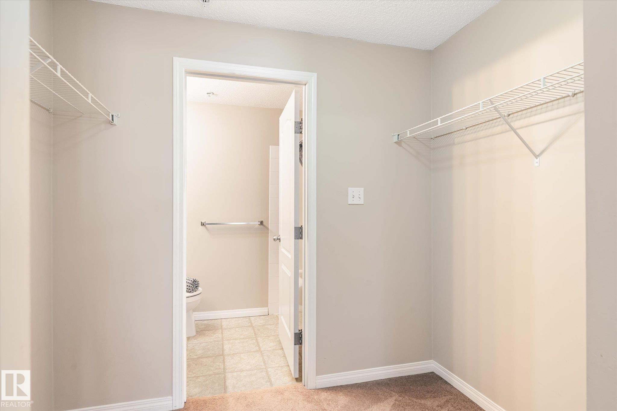 Carpeted area featuring two wire shelving units - 203 155 Edwards Drive, Edmonton, AB - Indoor With Storage