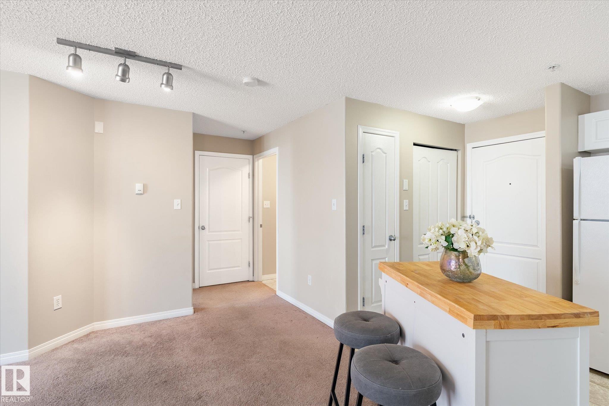 Open-concept living space featuring neutral paint, brown carpet, and a white kitchen island with a wood countertop - 203 155 Edwards Drive, Edmonton, AB - Indoor