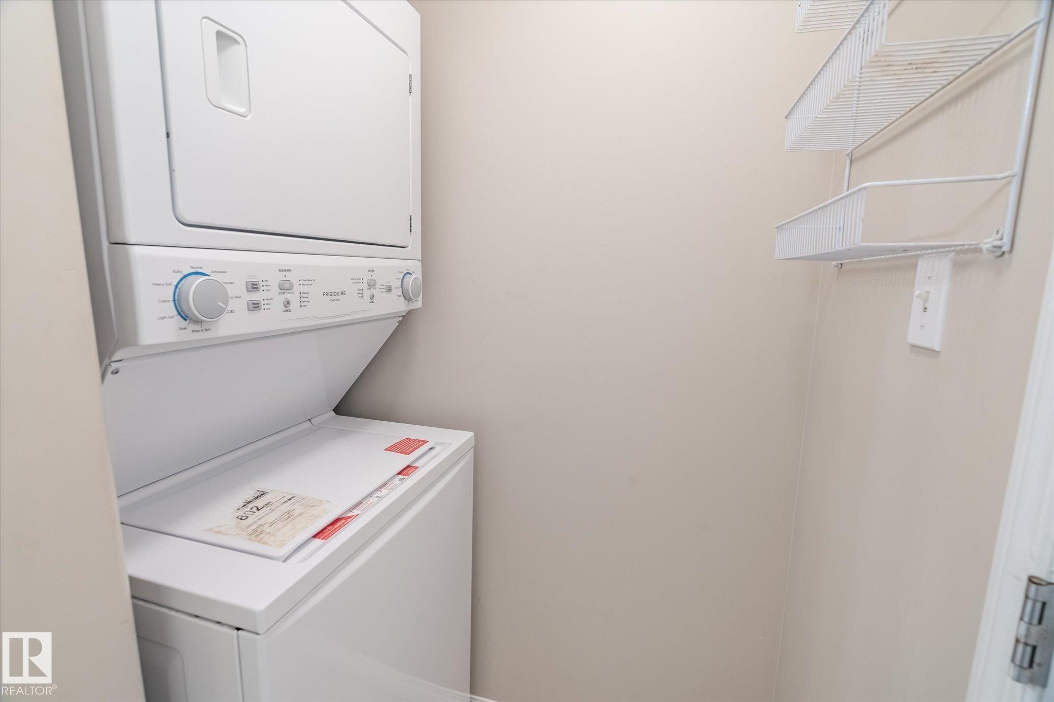 Dedicated laundry area featuring a stacked washer and dryer unit, and wall-mounted wire shelving - 203 155 Edwards Drive, Edmonton, AB - Indoor Photo Showing Laundry Room