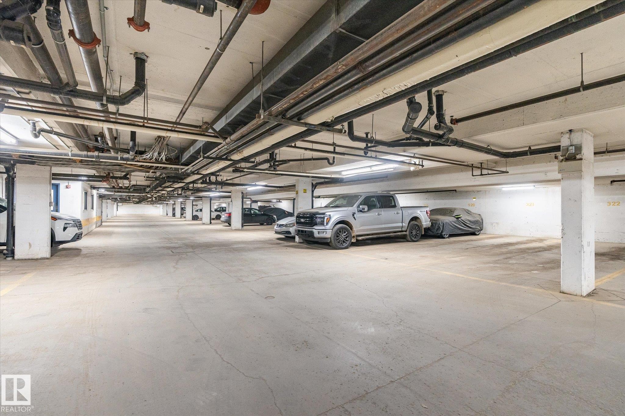 Expansive underground parking garage featuring concrete flooring, structural columns, and overhead lighting - 203 155 Edwards Drive, Edmonton, AB - Indoor Photo Showing Garage