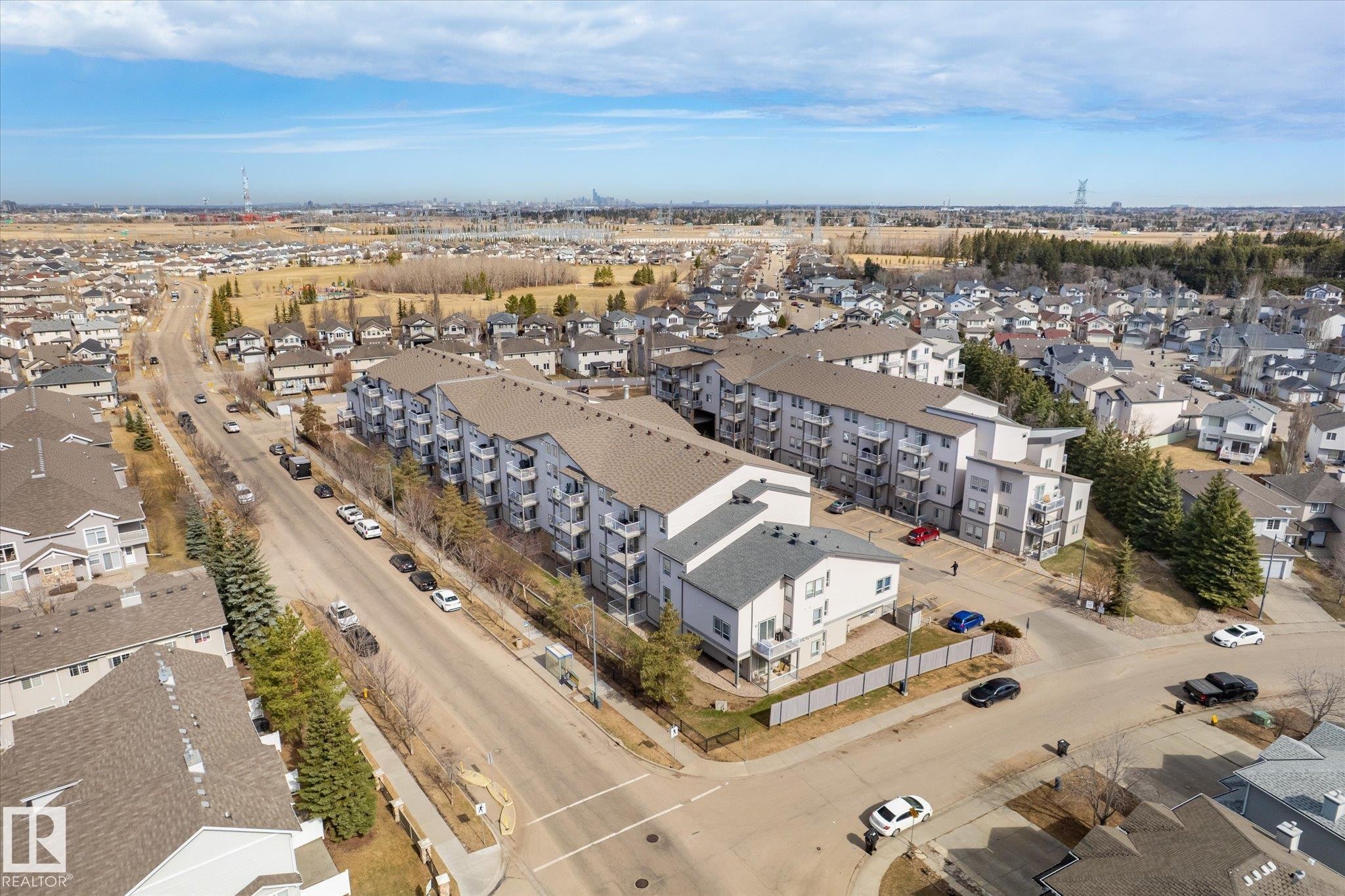 Contemporary multi-unit residential buildings featuring balconies and a neutral exterior palette, situated along a paved thoroughfare with street parking - 203 155 Edwards Drive, Edmonton, AB - Outdoor With View