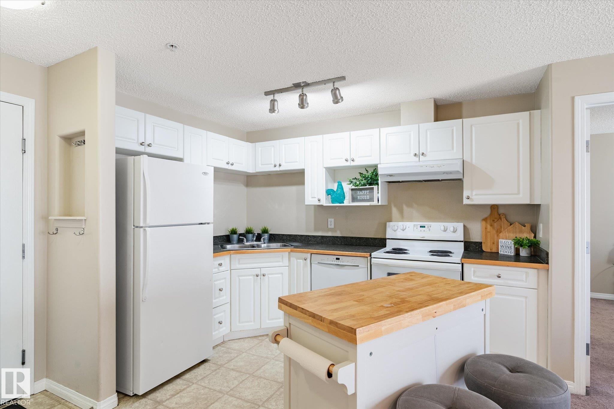 Efficient kitchen featuring white cabinetry, dark countertops, and tile flooring - 203 155 Edwards Drive, Edmonton, AB - Indoor Photo Showing Kitchen