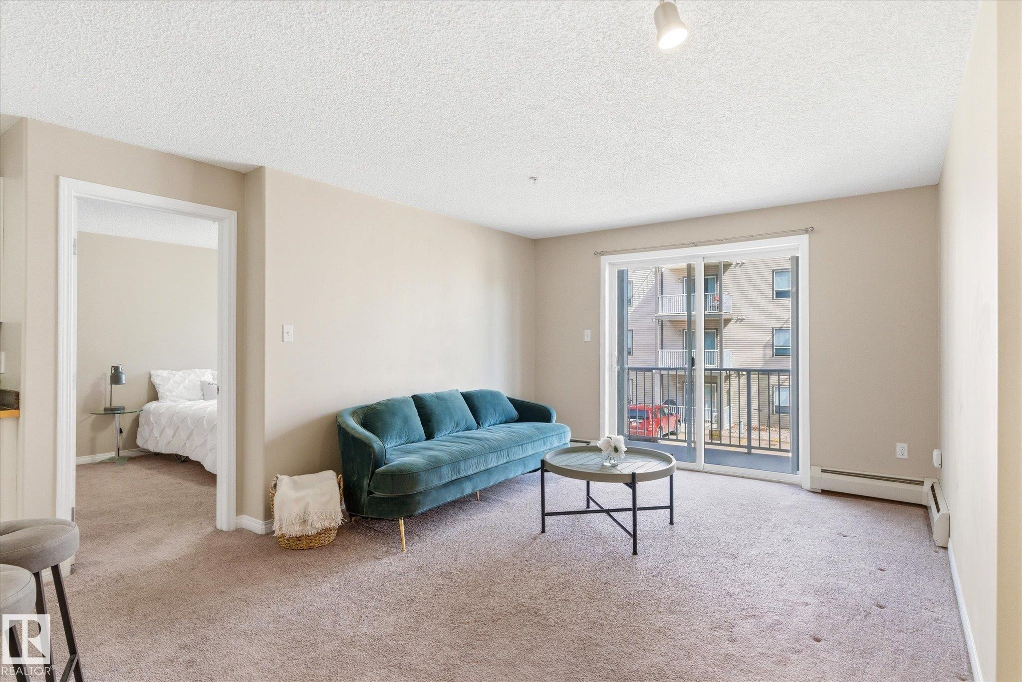 Living area featuring neutral wall tones, carpet flooring, a sliding glass door to a private balcony, track lighting, and white trim - 203 155 Edwards Drive, Edmonton, AB - Indoor Photo Showing Living Room