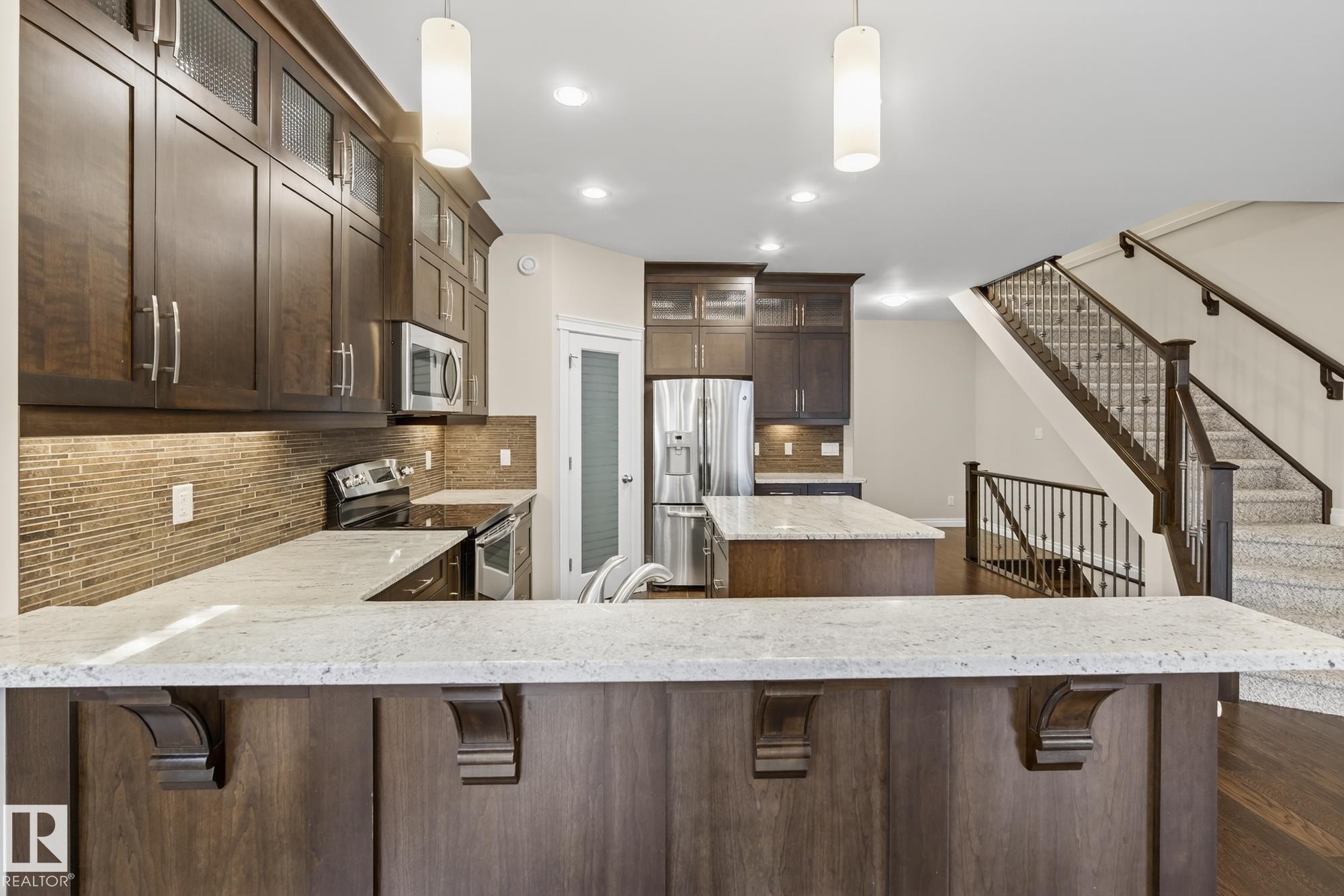 Kitchen featuring dark wood cabinetry, light-toned countertops, a mosaic tile backsplash, stainless steel appliances, and a central island - 11106 76 Avenue, Edmonton, AB - Indoor Photo Showing Kitchen With Stainless Steel Kitchen With Upgraded Kitchen