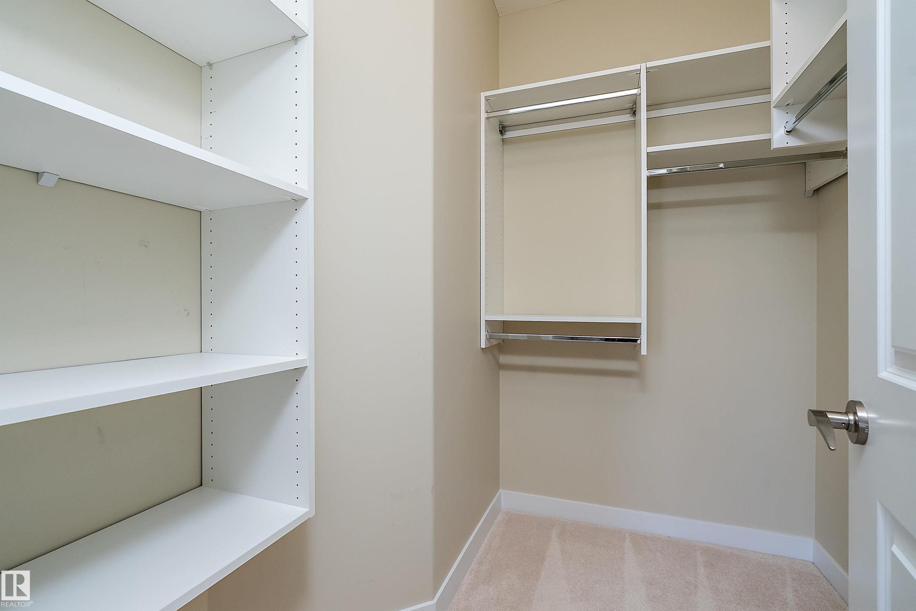 Built-in closet system with adjustable white shelving, multiple hanging rods, and neutral carpet flooring - 14 3090 Cameron Heights Way, Edmonton, AB - Indoor With Storage