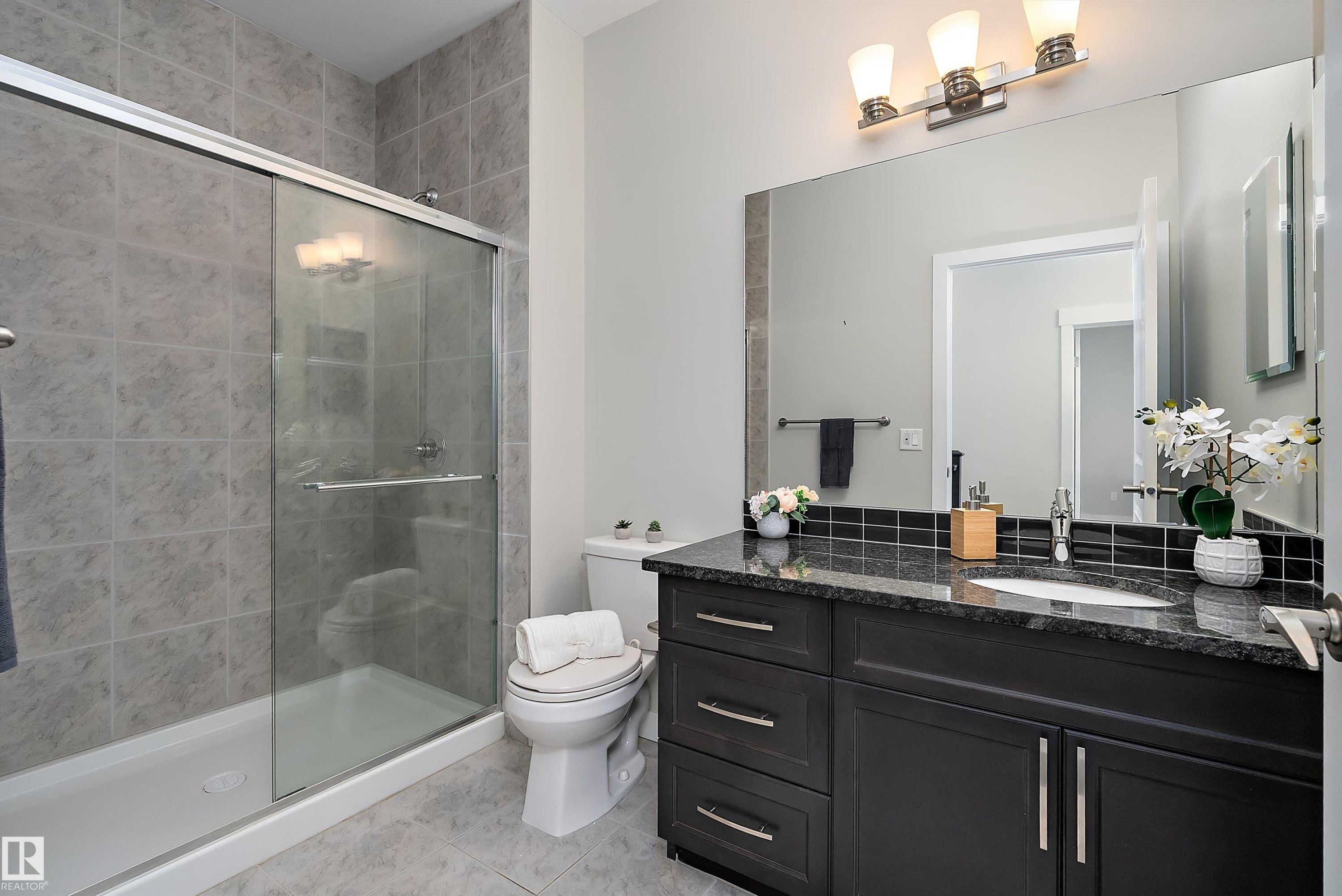 Bathroom featuring a dark wood-finish vanity with a stone countertop, a white rectangular sink, and a large wall-mounted mirror - 14 3090 Cameron Heights Way, Edmonton, AB - Indoor Photo Showing Bathroom