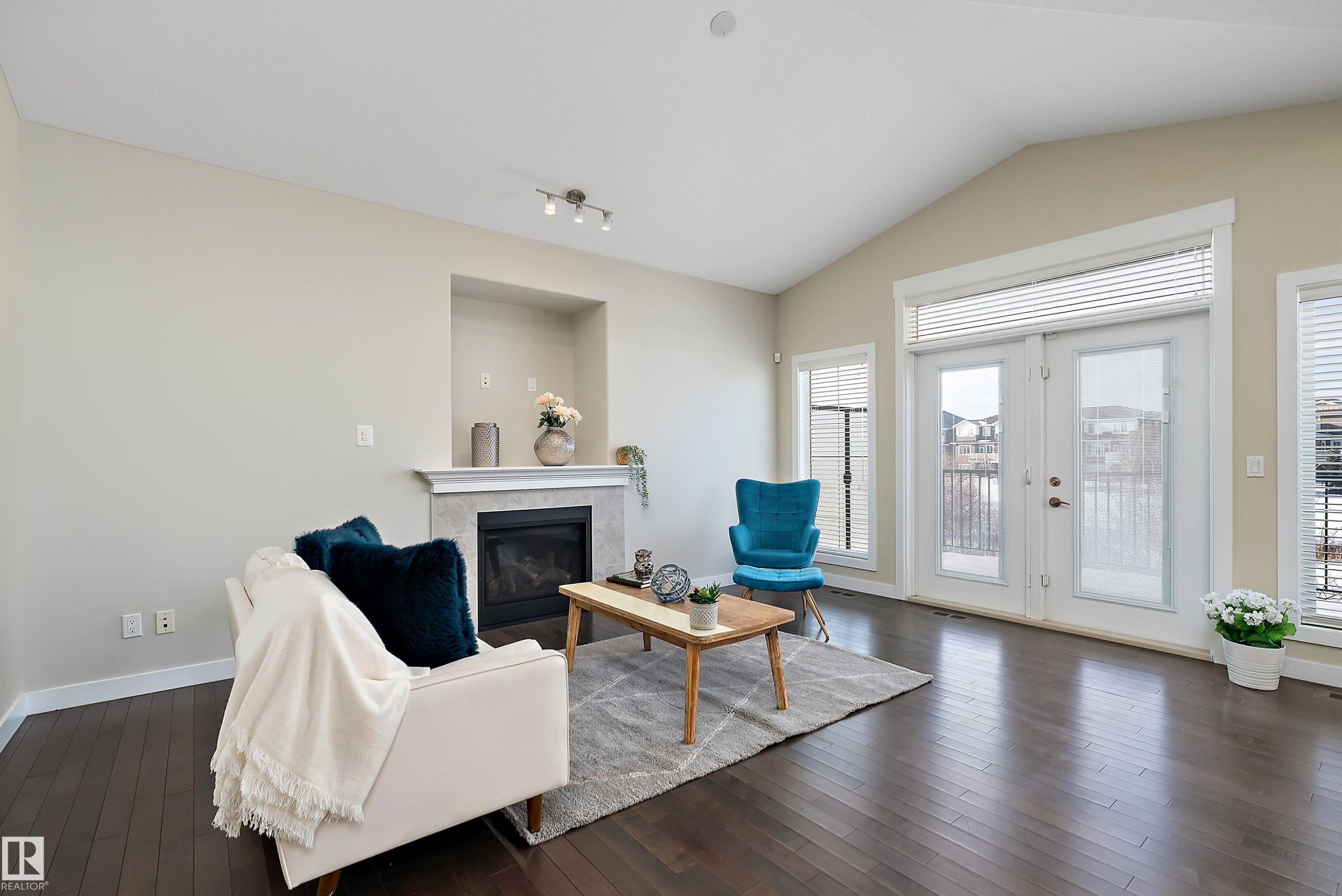 Living area featuring vaulted ceilings, dark wood-finish flooring, a built-in fireplace with a stone surround and mantel, and French doors with transom windows - 14 3090 Cameron Heights Way, Edmonton, AB - Indoor Photo Showing Living Room With Fireplace