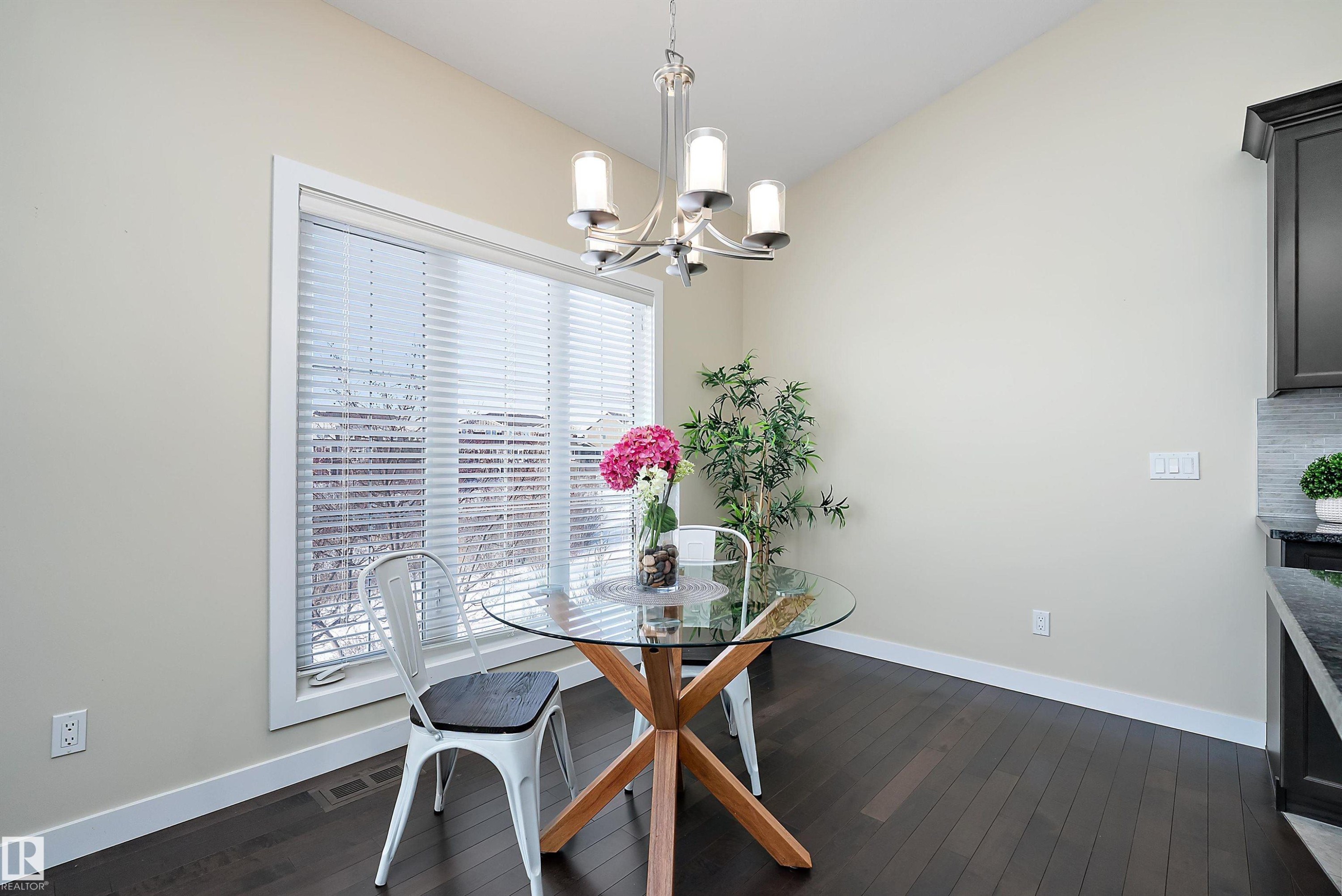 Dining area featuring dark wood-finish flooring, a large window with blinds, and a contemporary chandelier - 14 3090 Cameron Heights Way, Edmonton, AB - Indoor Photo Showing Dining Room