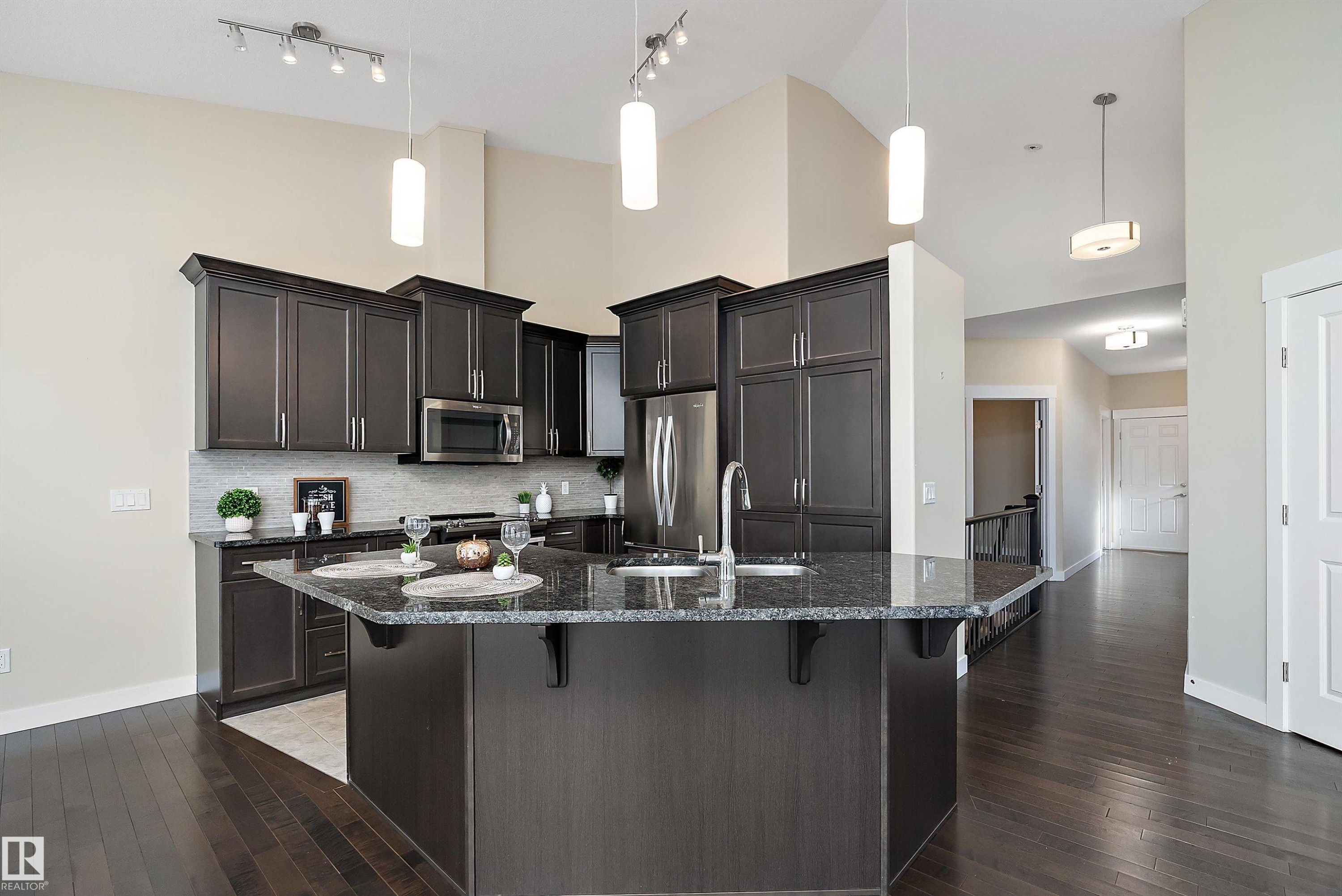 Modern kitchen featuring a large central island with a dark countertop and undermount sink - 14 3090 Cameron Heights Way, Edmonton, AB - Indoor Photo Showing Kitchen With Upgraded Kitchen